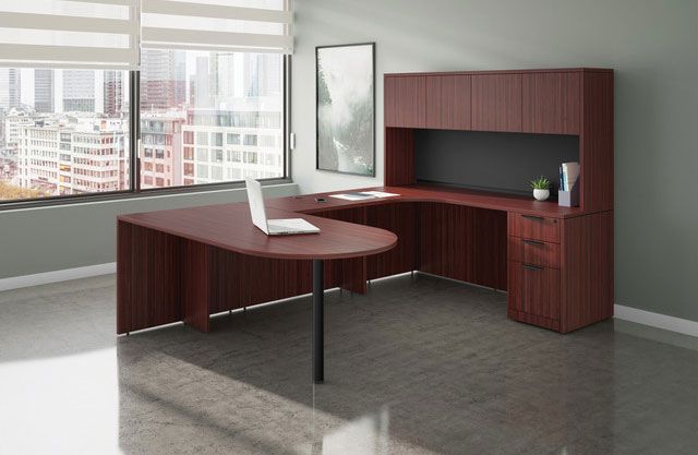 L-shaped maroon office desk with overhead storage in a room with a window and a laptop.