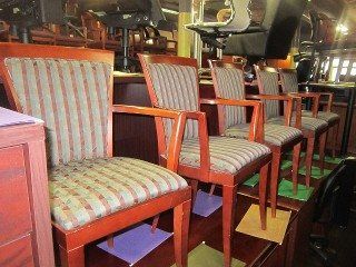 Four wooden chairs with striped cushions and armrests in a row near a bar.