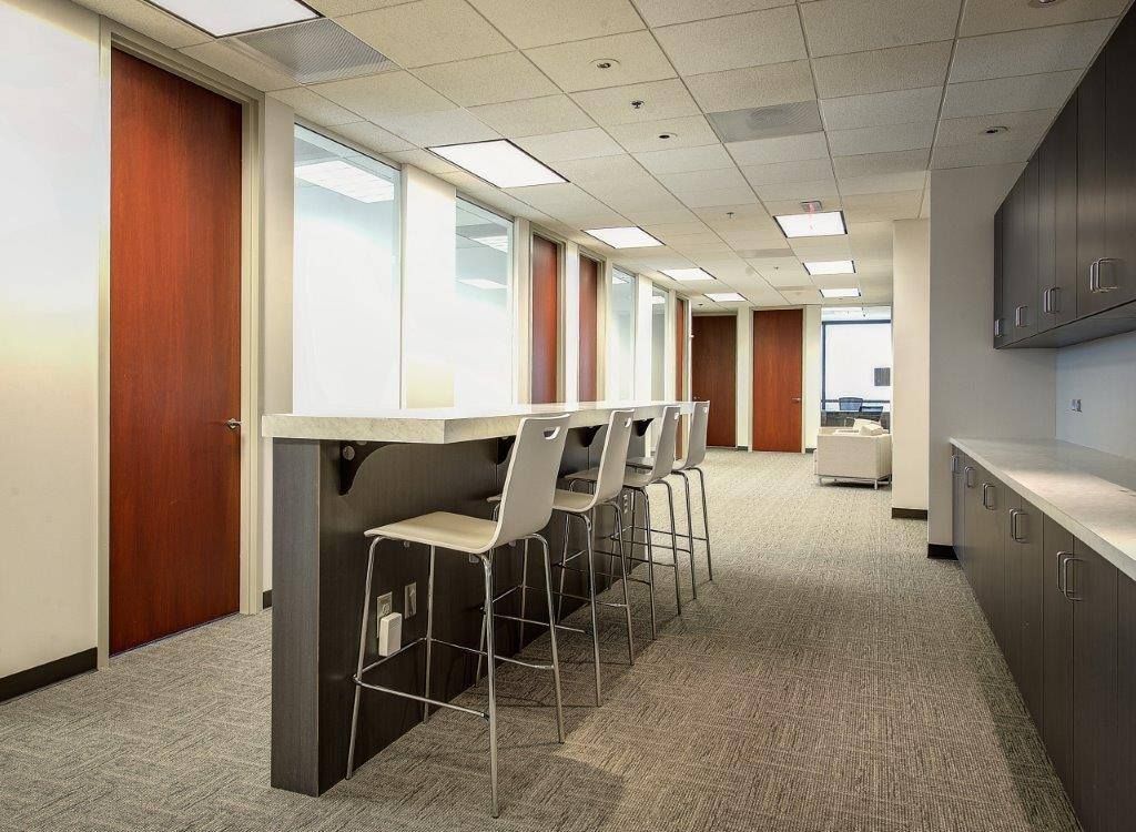 Office break room with a counter, stools, windows, and cabinets.