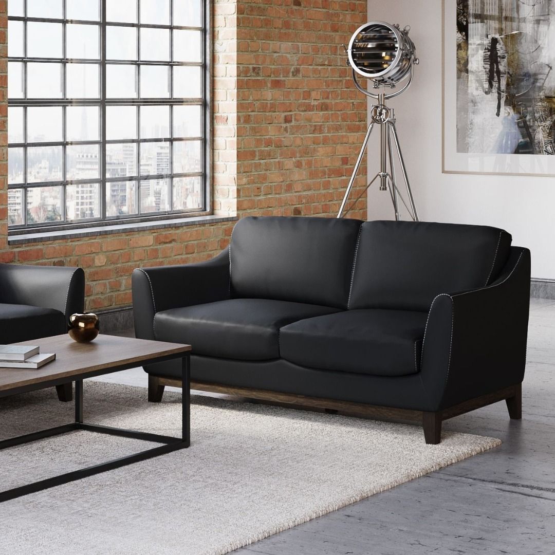 Black leather loveseat in a modern living room with a rug, brick wall, and window.