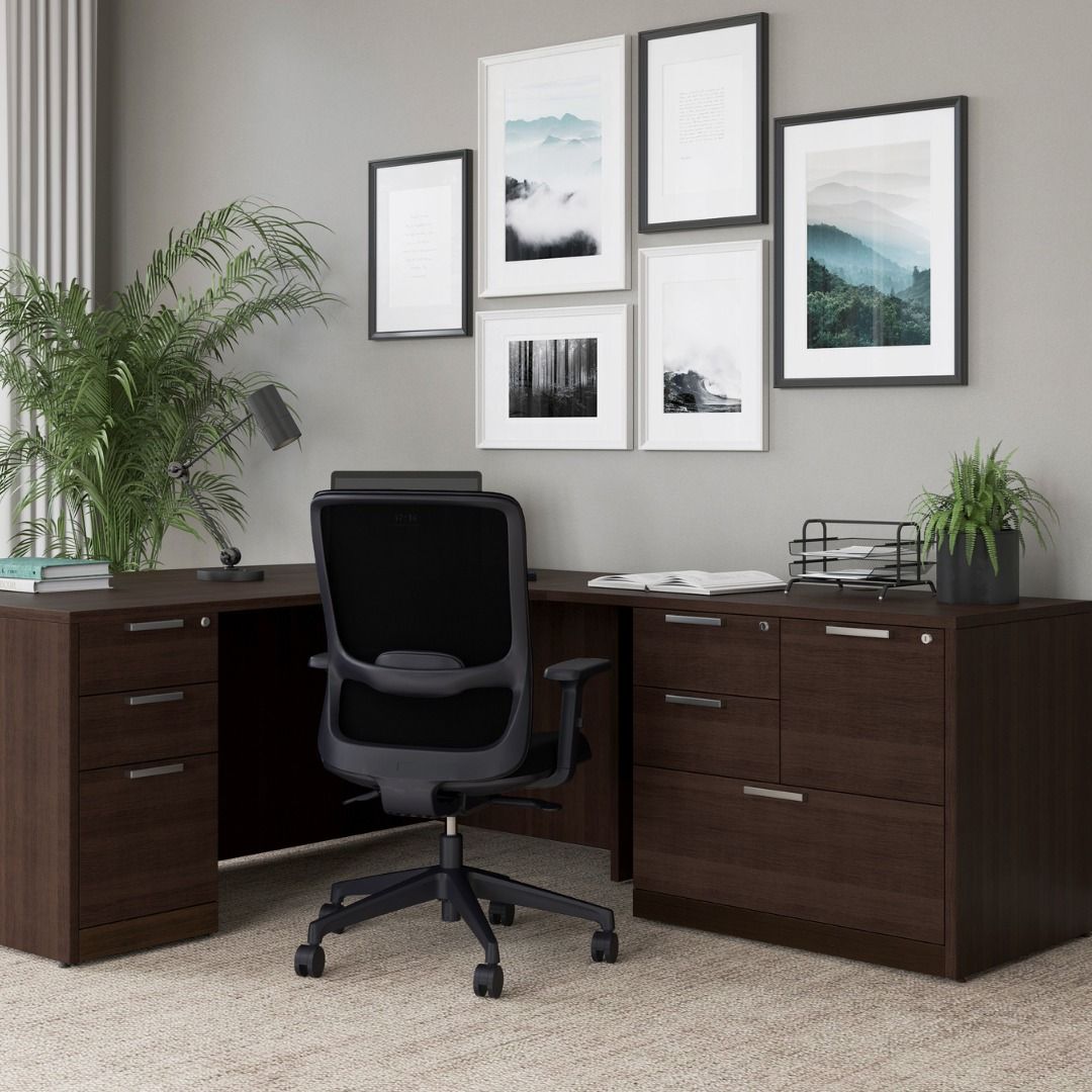 Brown desk with black chair, against gray wall with framed art and small plants.