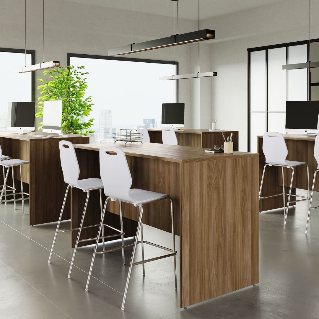 Modern office with wooden desks, white bar stools, and computers. Large windows offer a bright workspace.