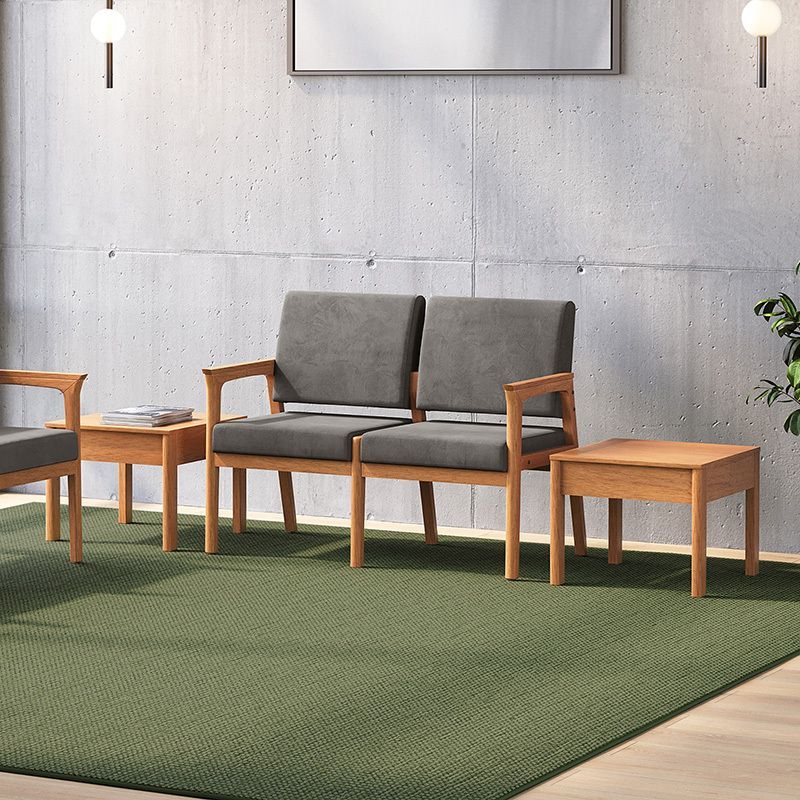 Waiting area with gray loveseat, wooden end tables, and green carpet against a concrete wall.