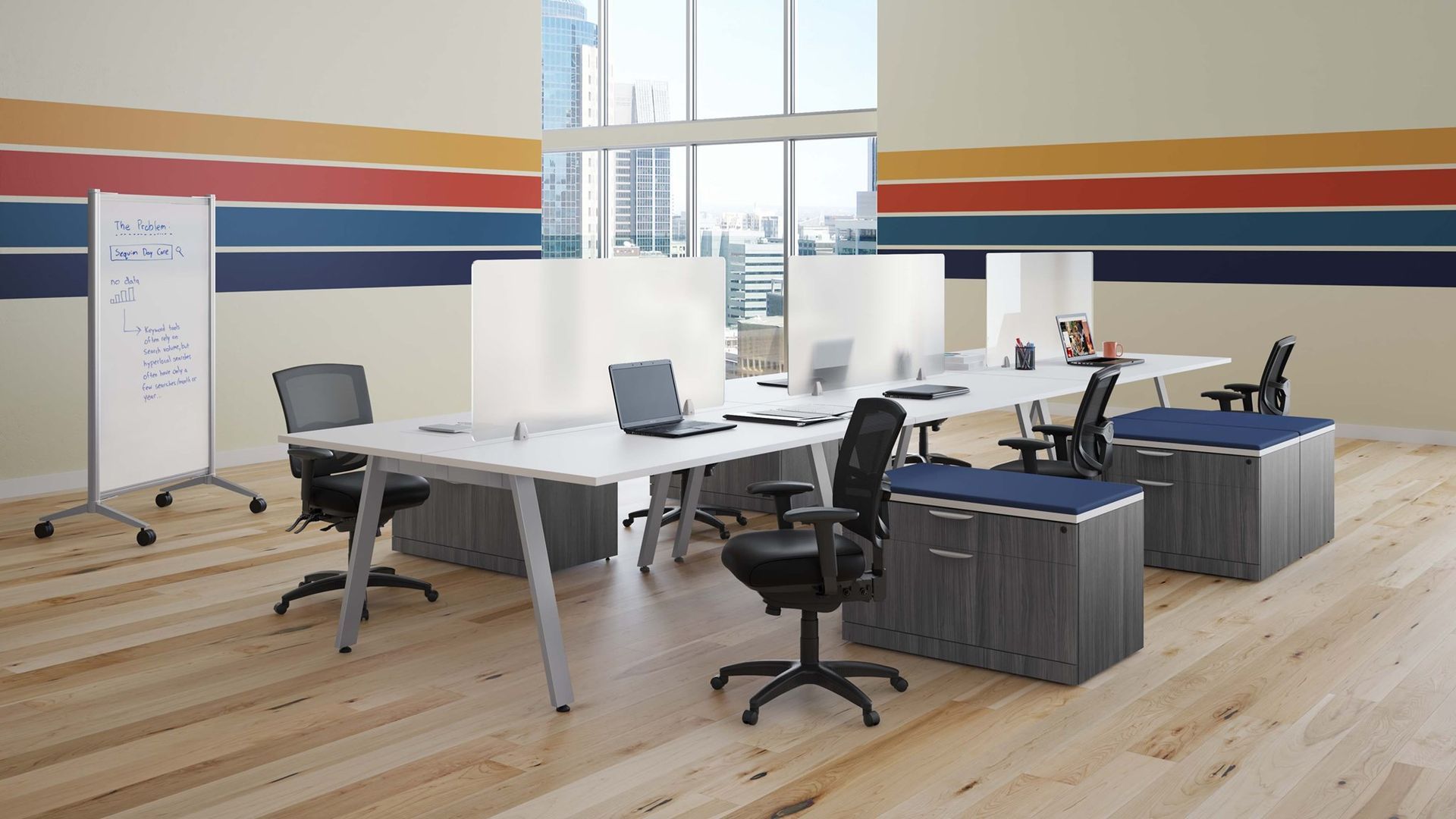 Office space with desks, chairs, and dividers; a whiteboard on the left, windows and colorful wall design.