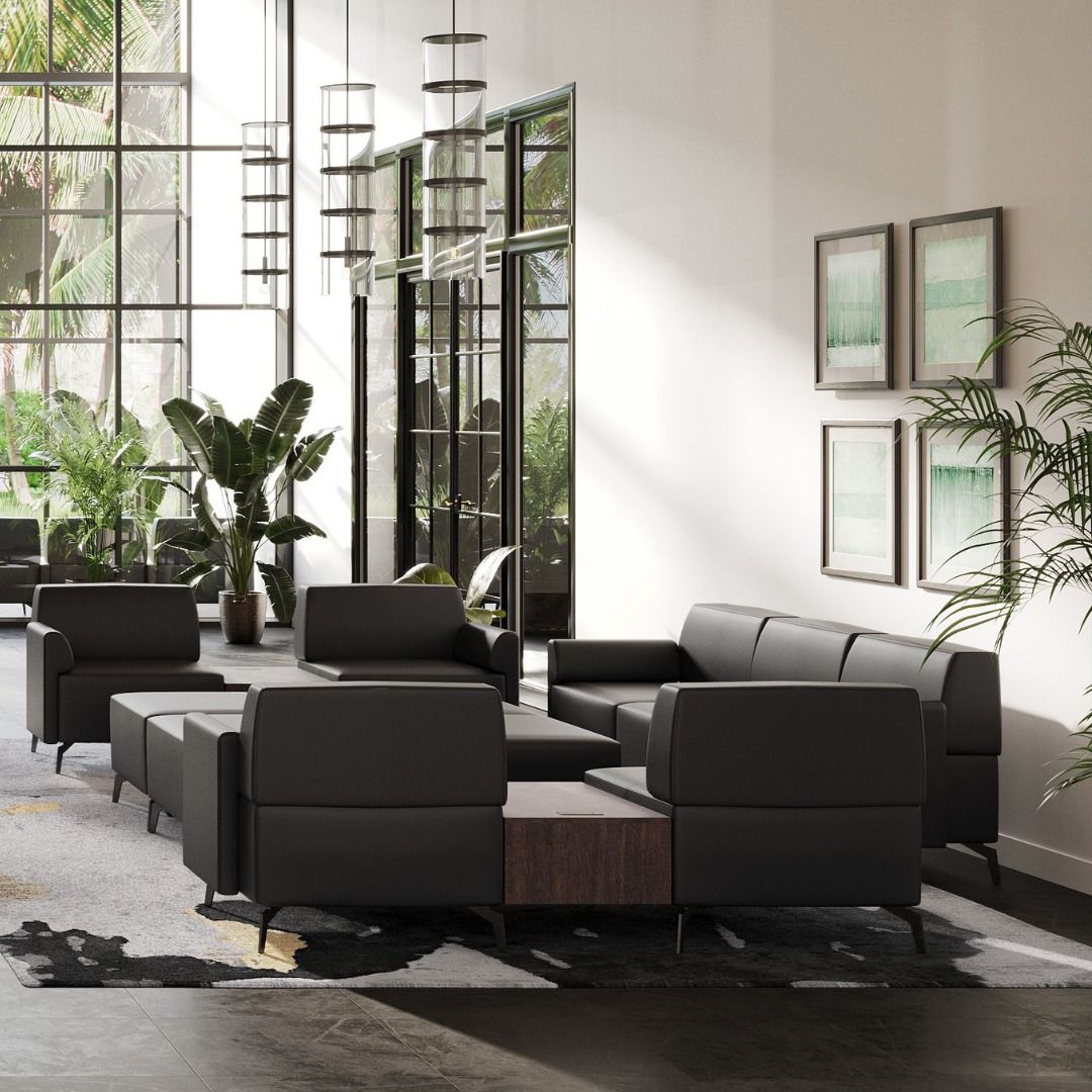 Modern office lounge area with black leather modular seating, wooden side table, large windows, and plants.