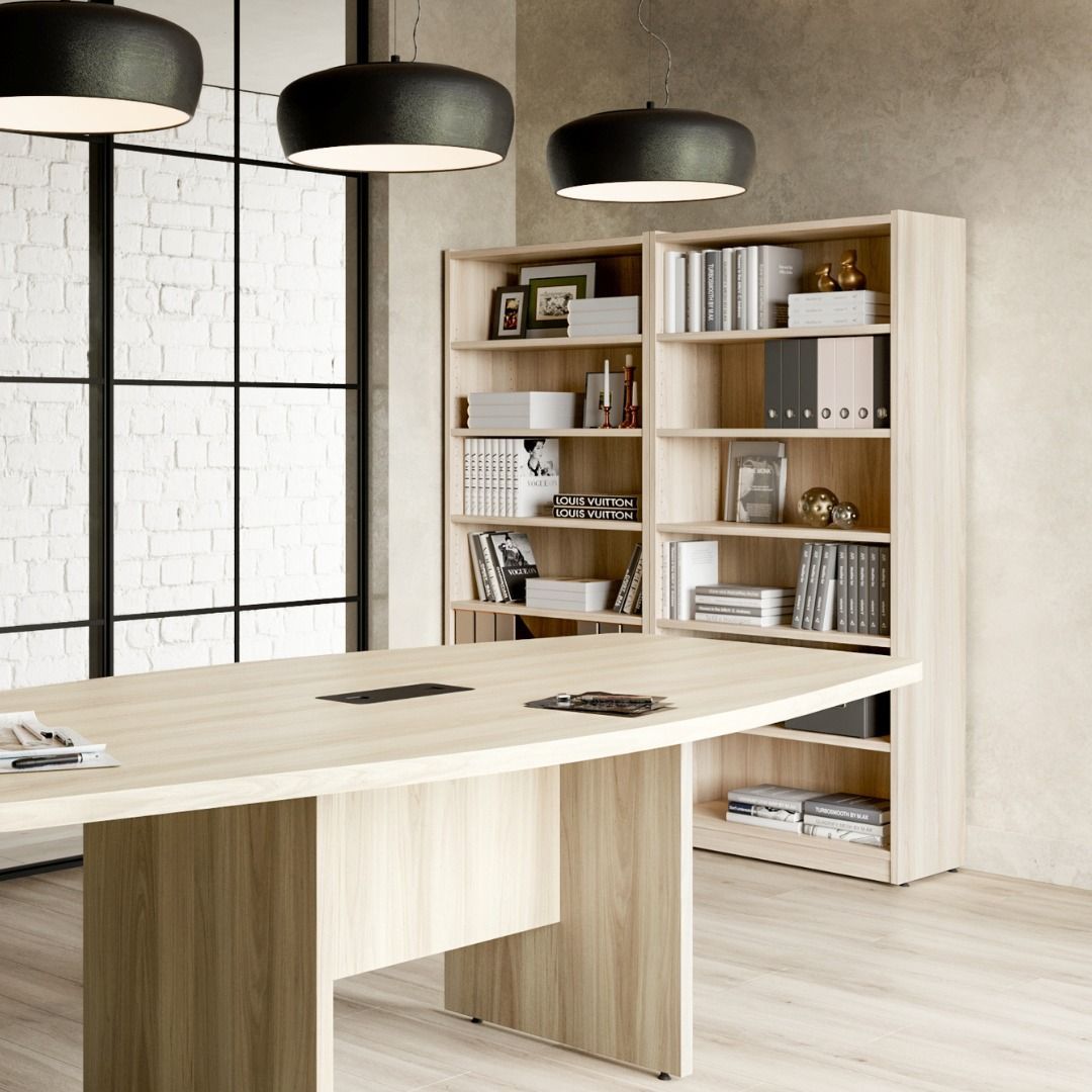 Office interior with a light wood conference table, bookshelves, and black pendant lights.