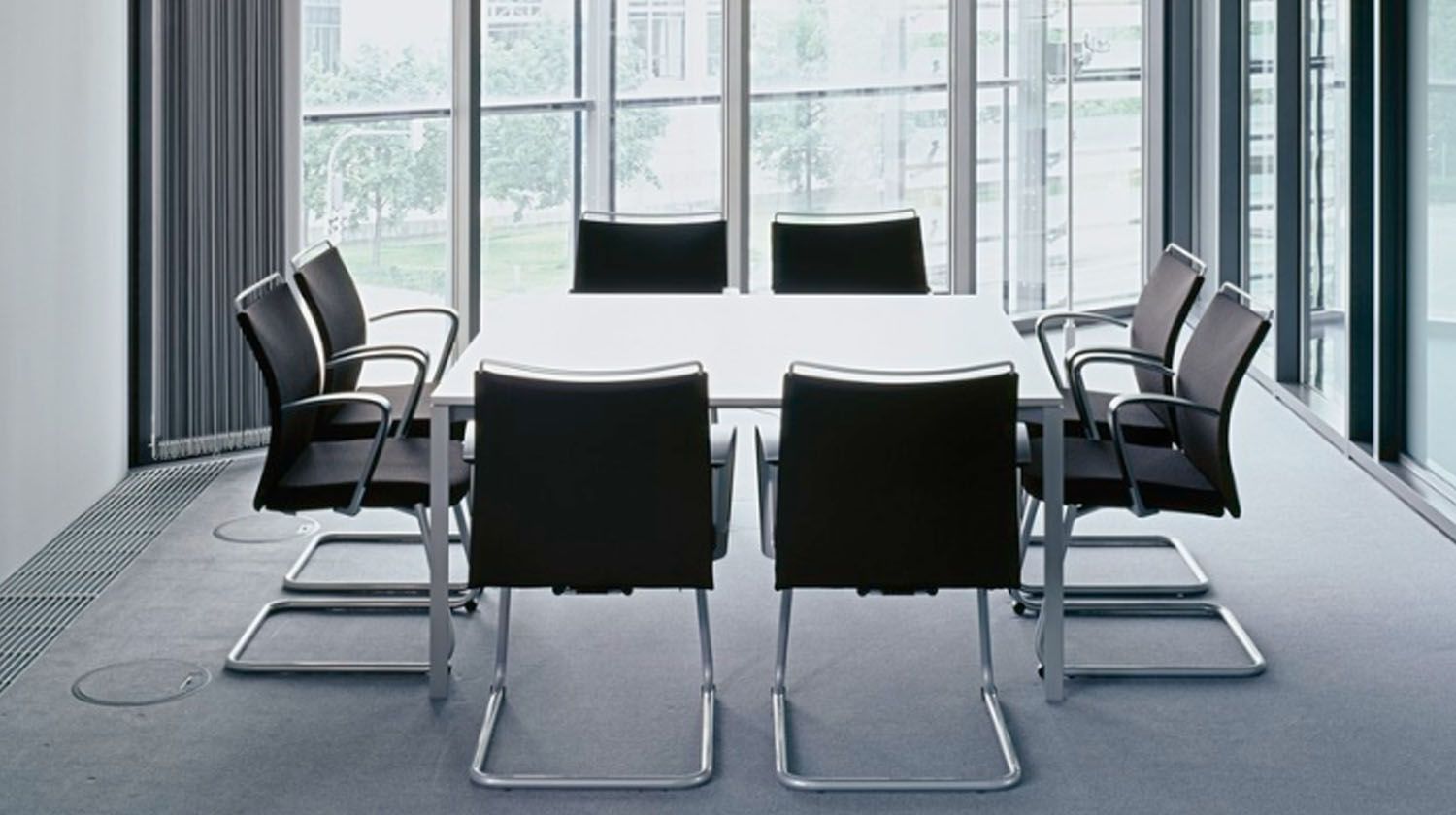 Conference room with white table and black chairs, large windows.