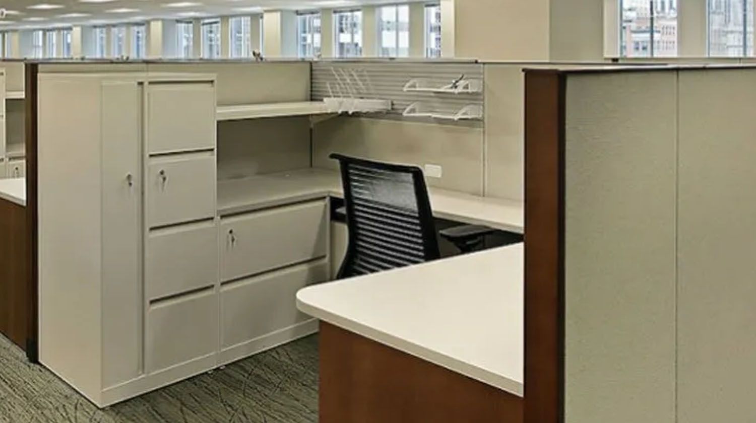 Office cubicle with white desk, cabinets, and a black office chair.