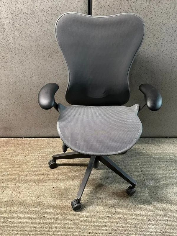 Black ergonomic office chair on a patterned rug, against a gray wall.