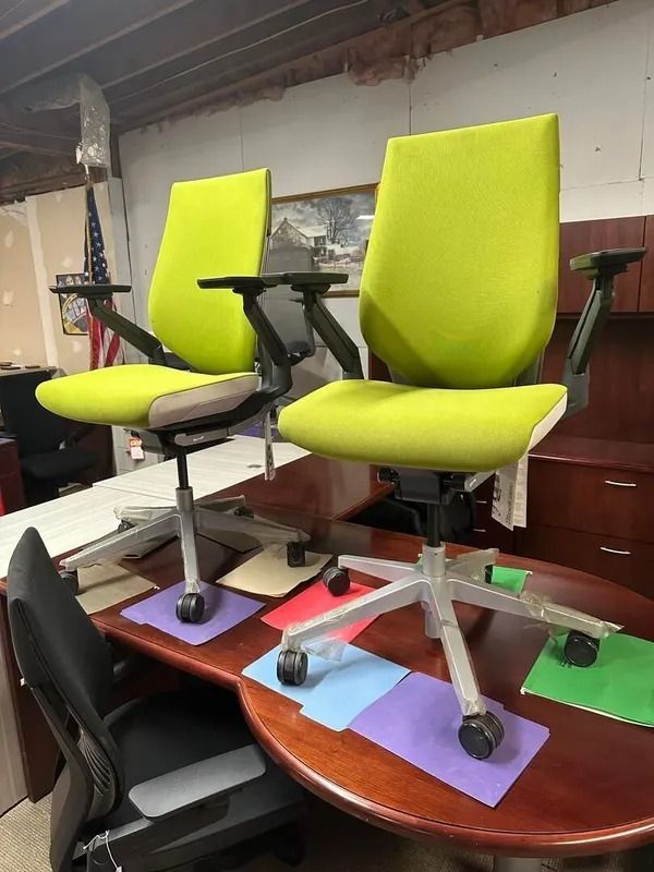 Two lime green office chairs on a wooden desk with black armrests and a silver base.
