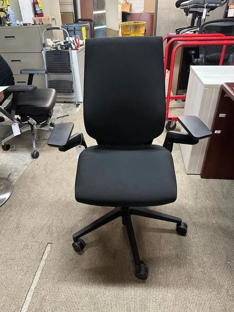 Black office chair with adjustable armrests on a patterned carpet.