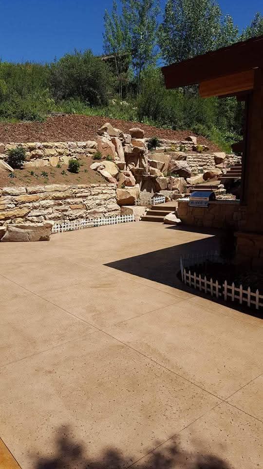 A patio with a stone wall and a waterfall in the background.