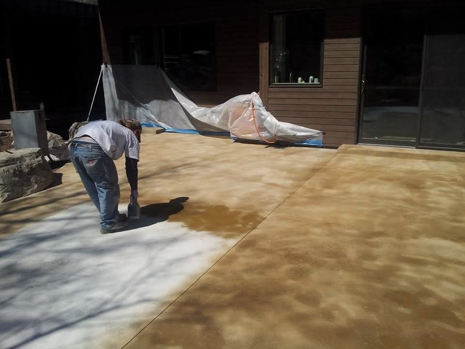 A man is painting a concrete patio in front of a house
