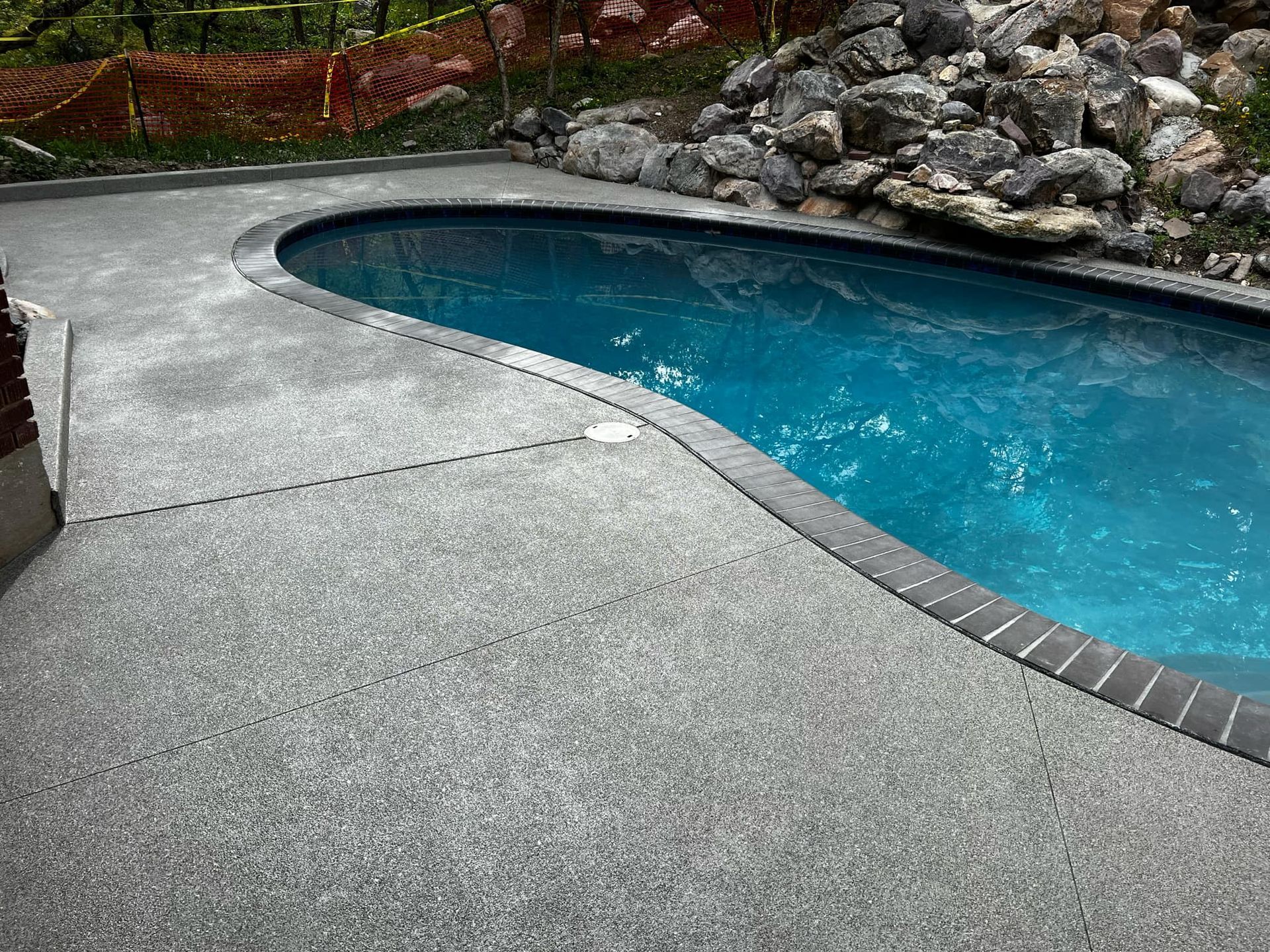 A large swimming pool is surrounded by rocks and a concrete deck.