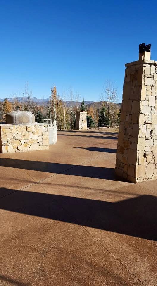 A driveway with a stone wall and pillars on a sunny day.