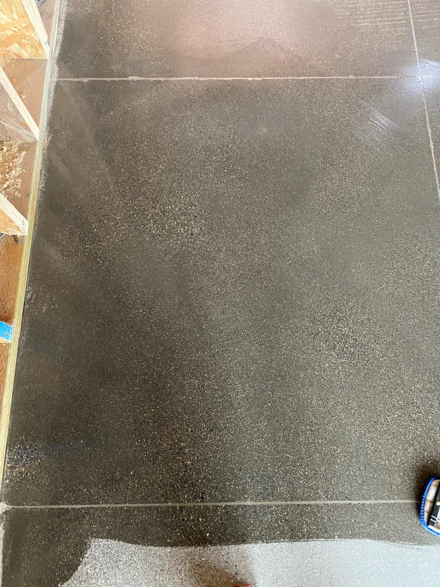 A close up of a black concrete floor with a blue tape measure on it.