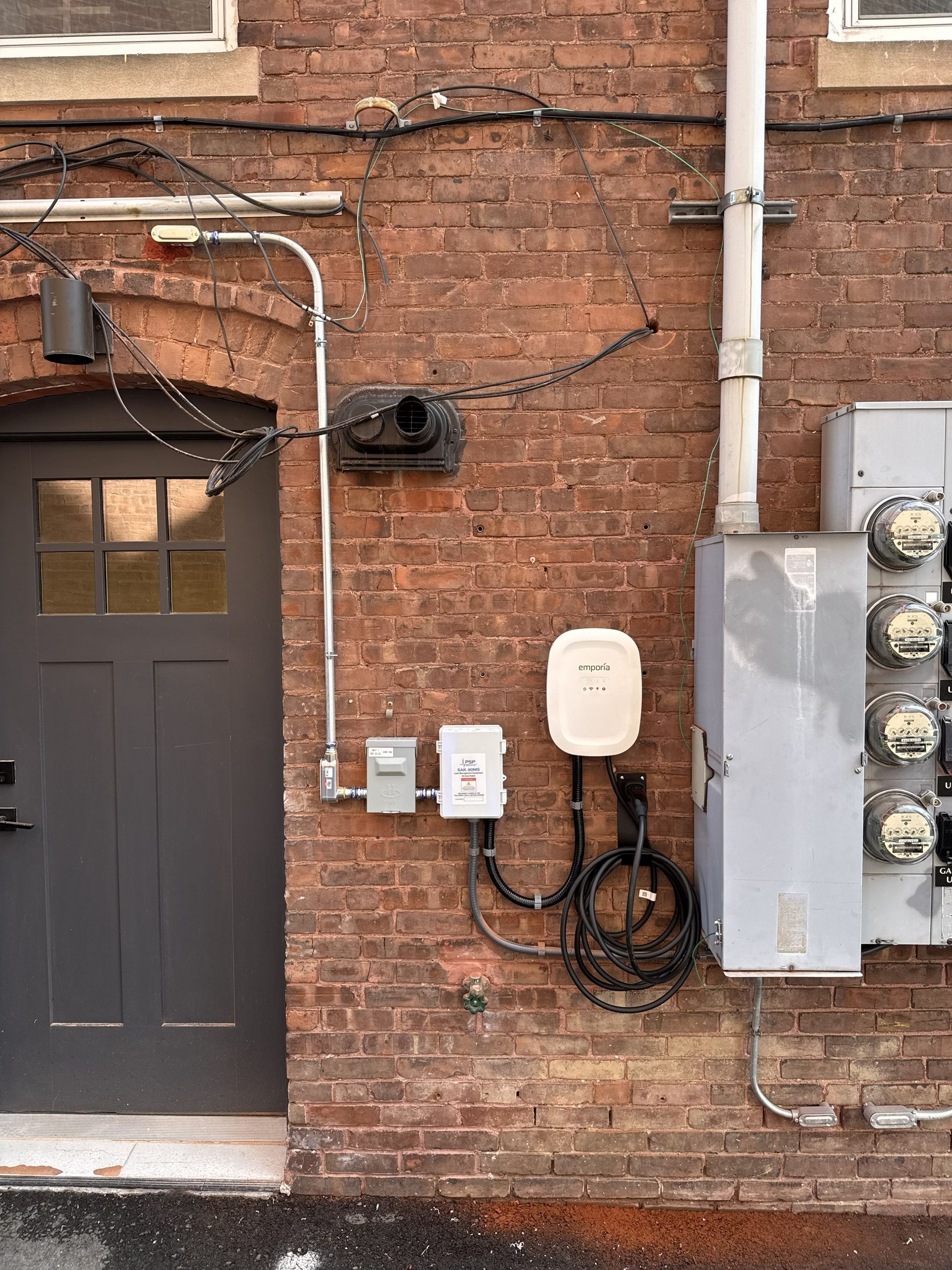Brick wall with door, utility meters, and electrical boxes beside an alley entrance