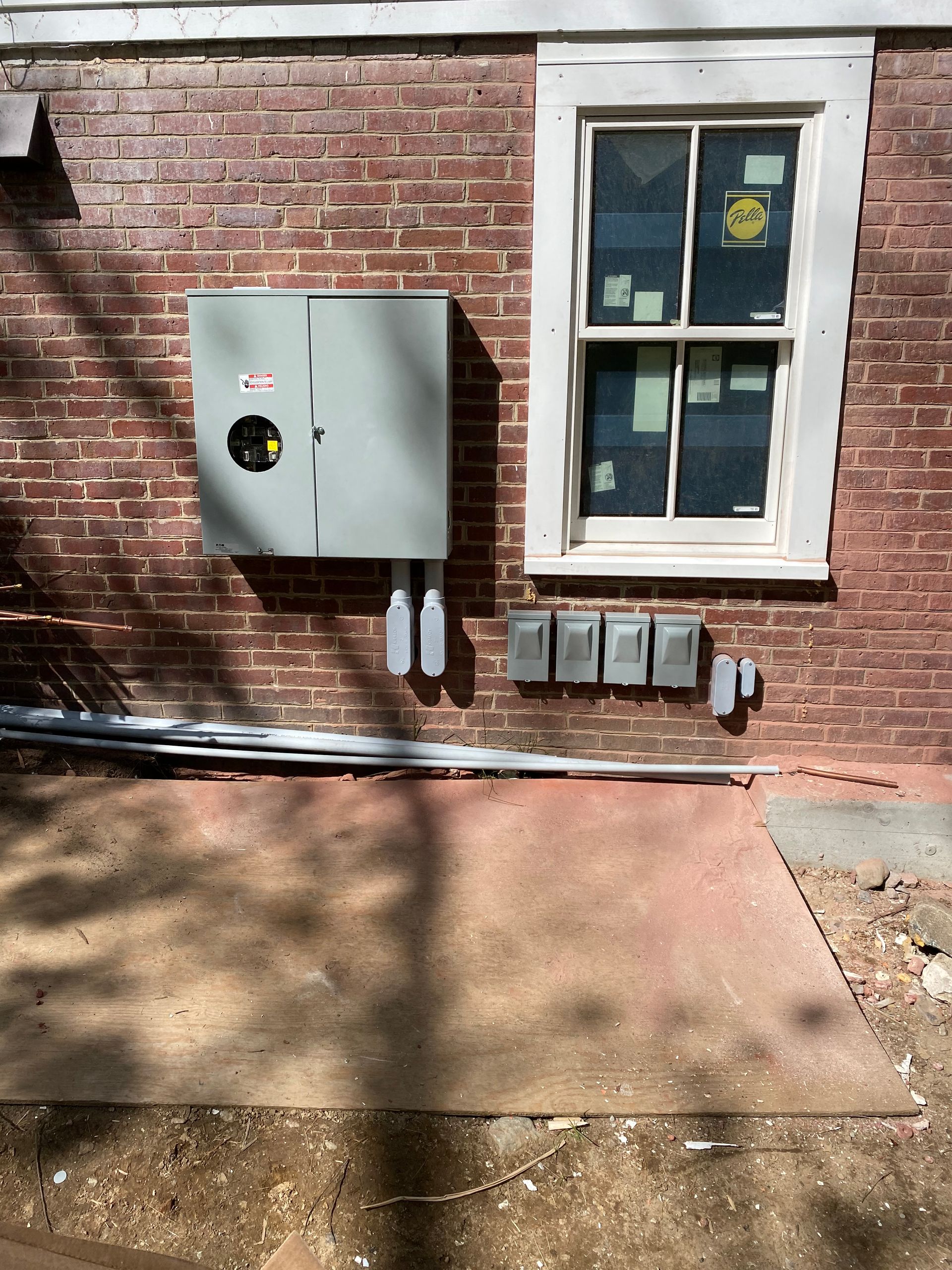 Electrical box and conduit on brick wall next to a window; ground area painted red.