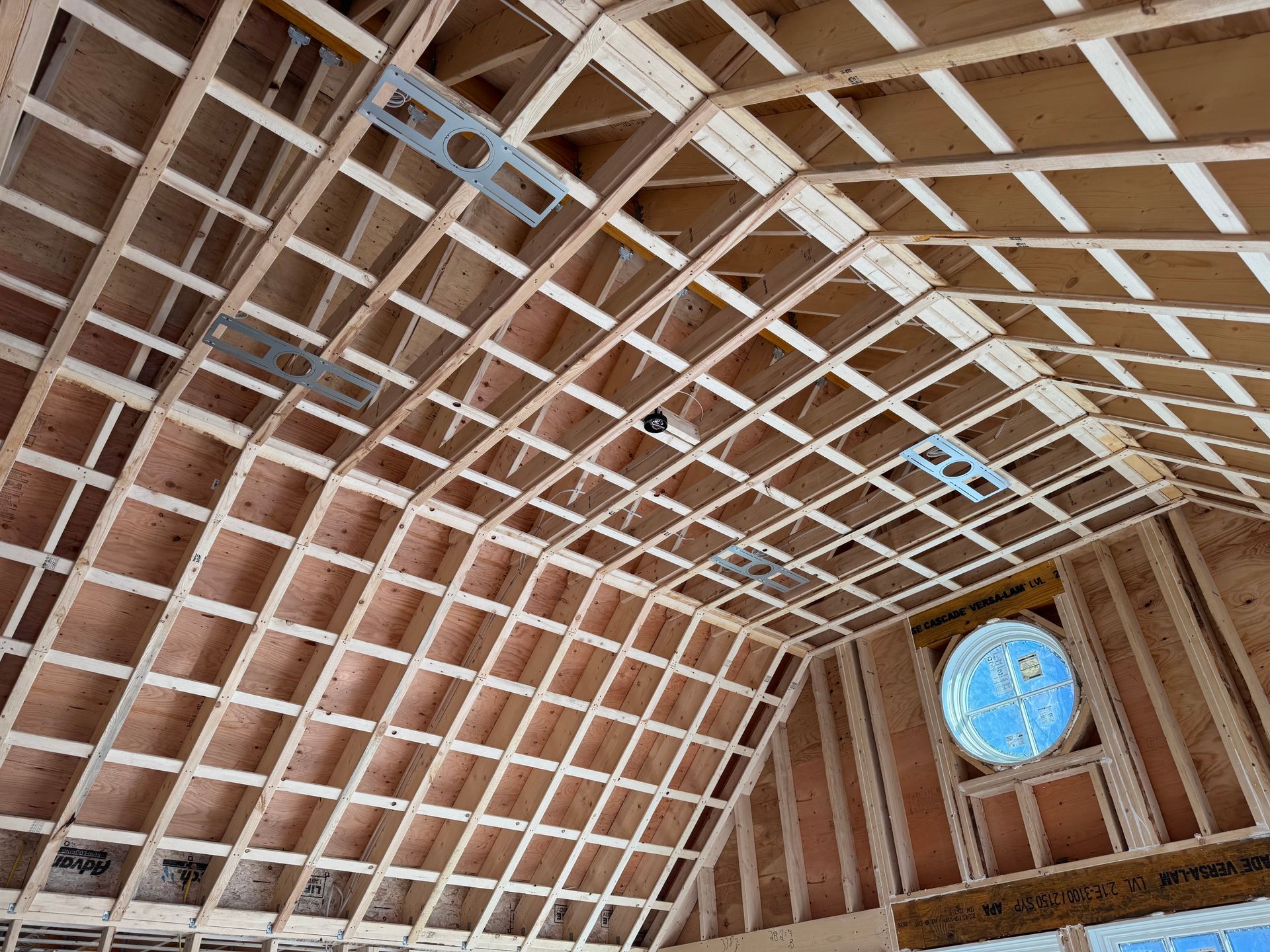 Wooden framework of a gabled roof and walls under construction. A circular, blue window is visible.