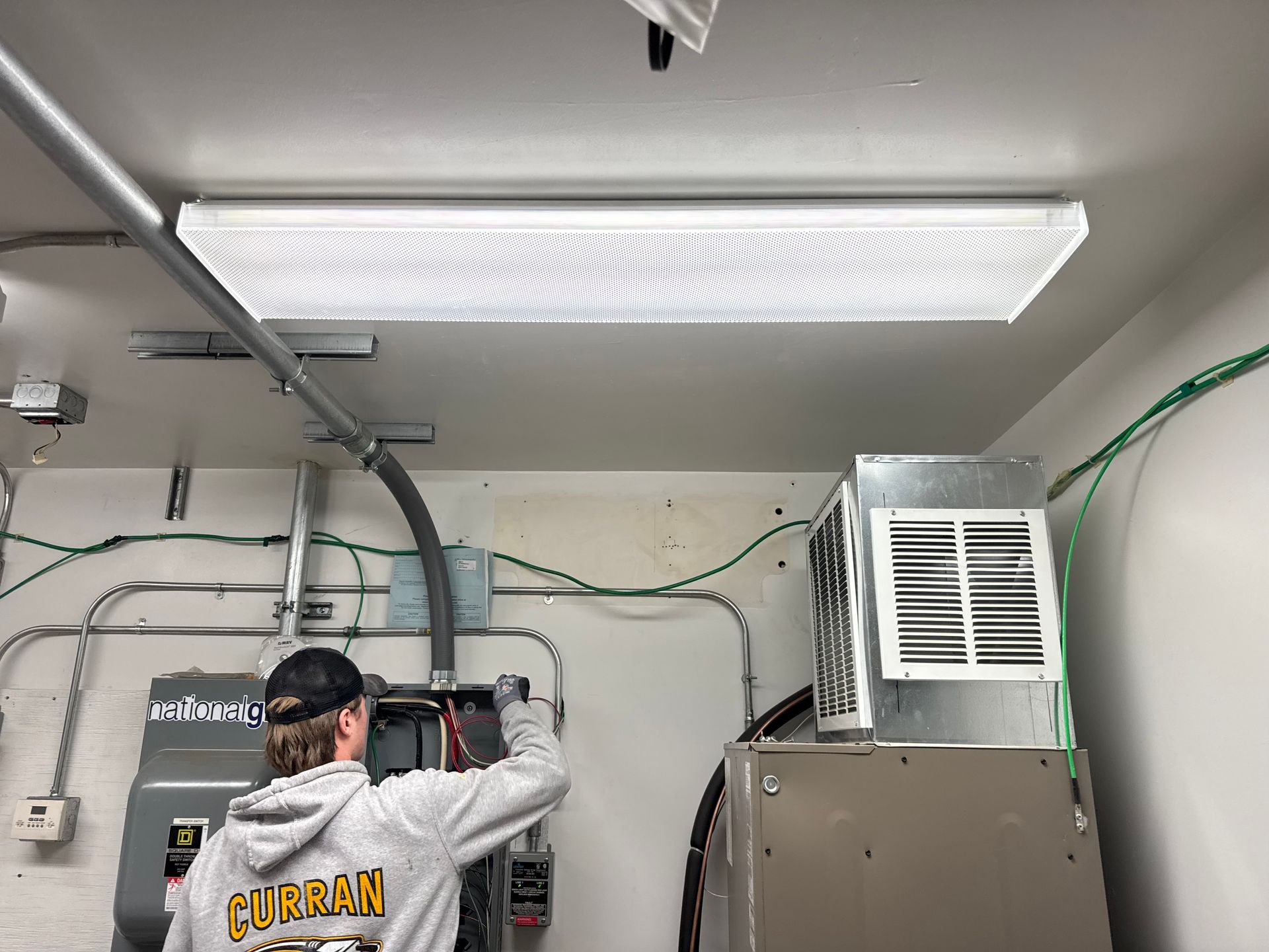 Man working on electrical panel in a garage, under a fluorescent light.