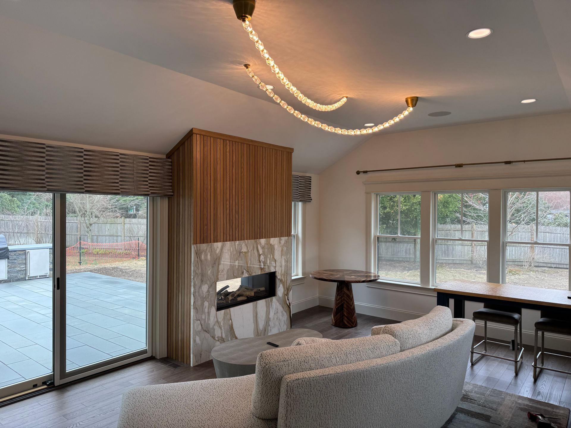 Living room with fireplace, sliding door to backyard, and curved sofa, and crystal light fixture.