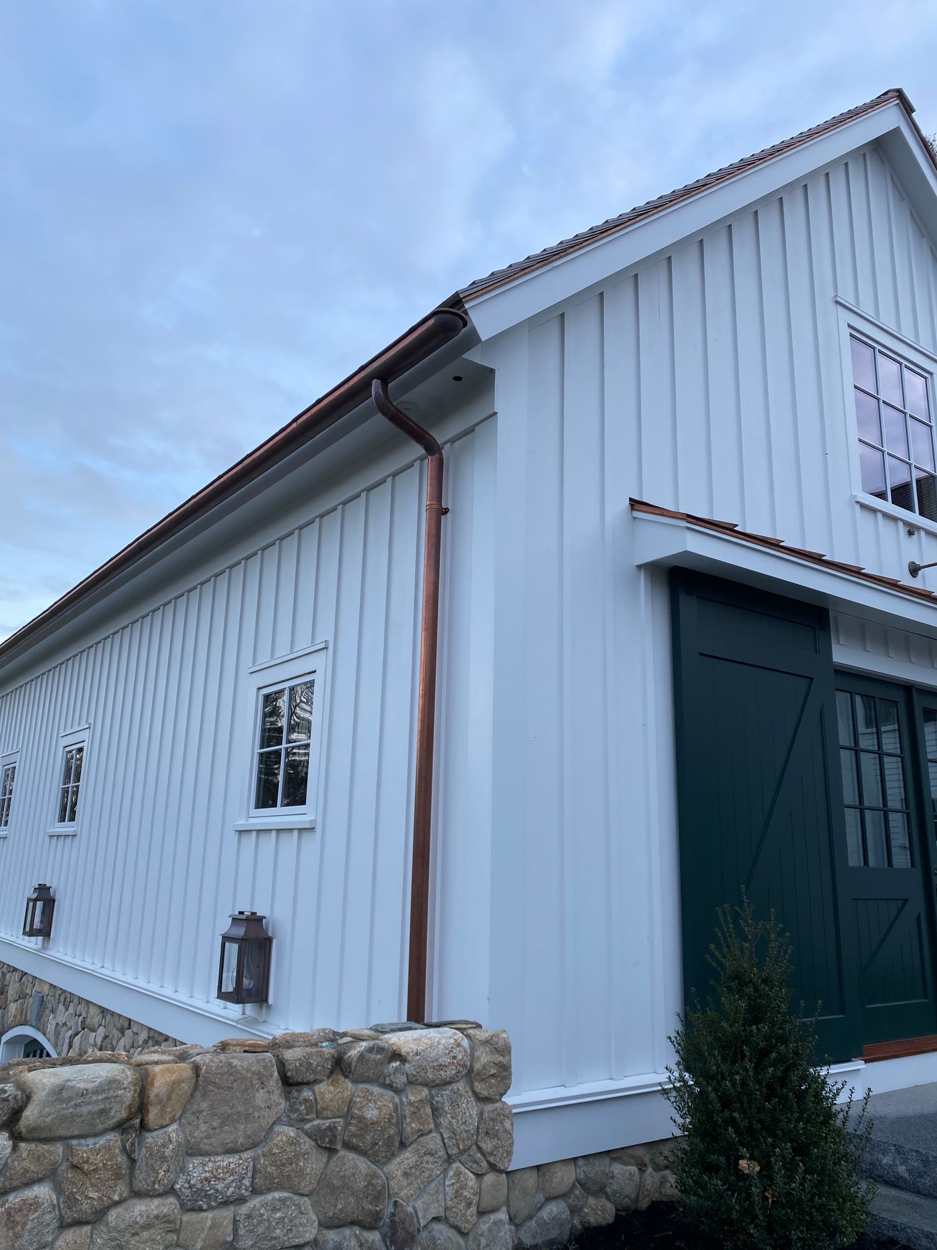 White farmhouse exterior with copper gutters and green sliding door.