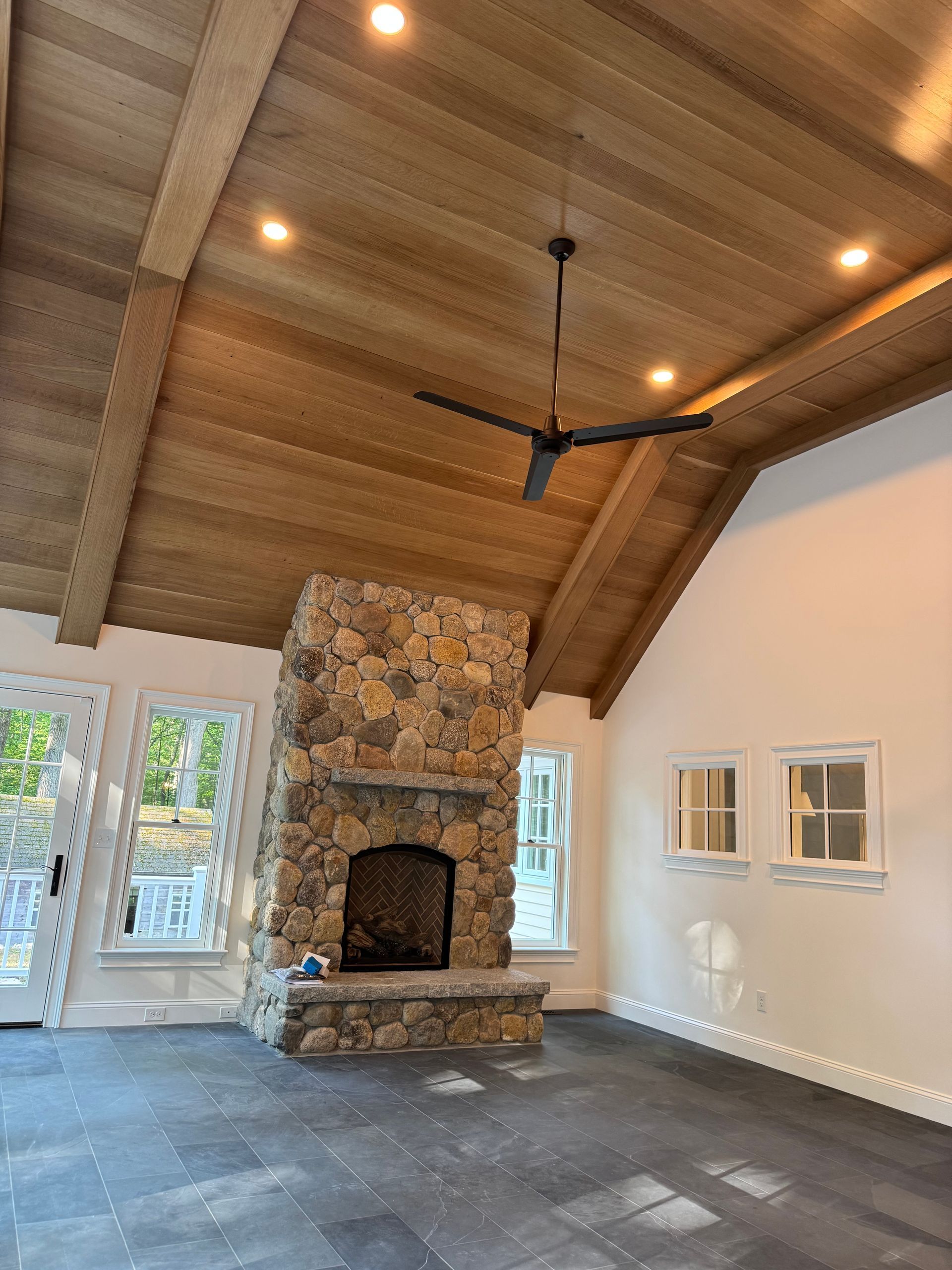 Stone fireplace in a room with a wood ceiling, recessed lighting, and a black ceiling fan.