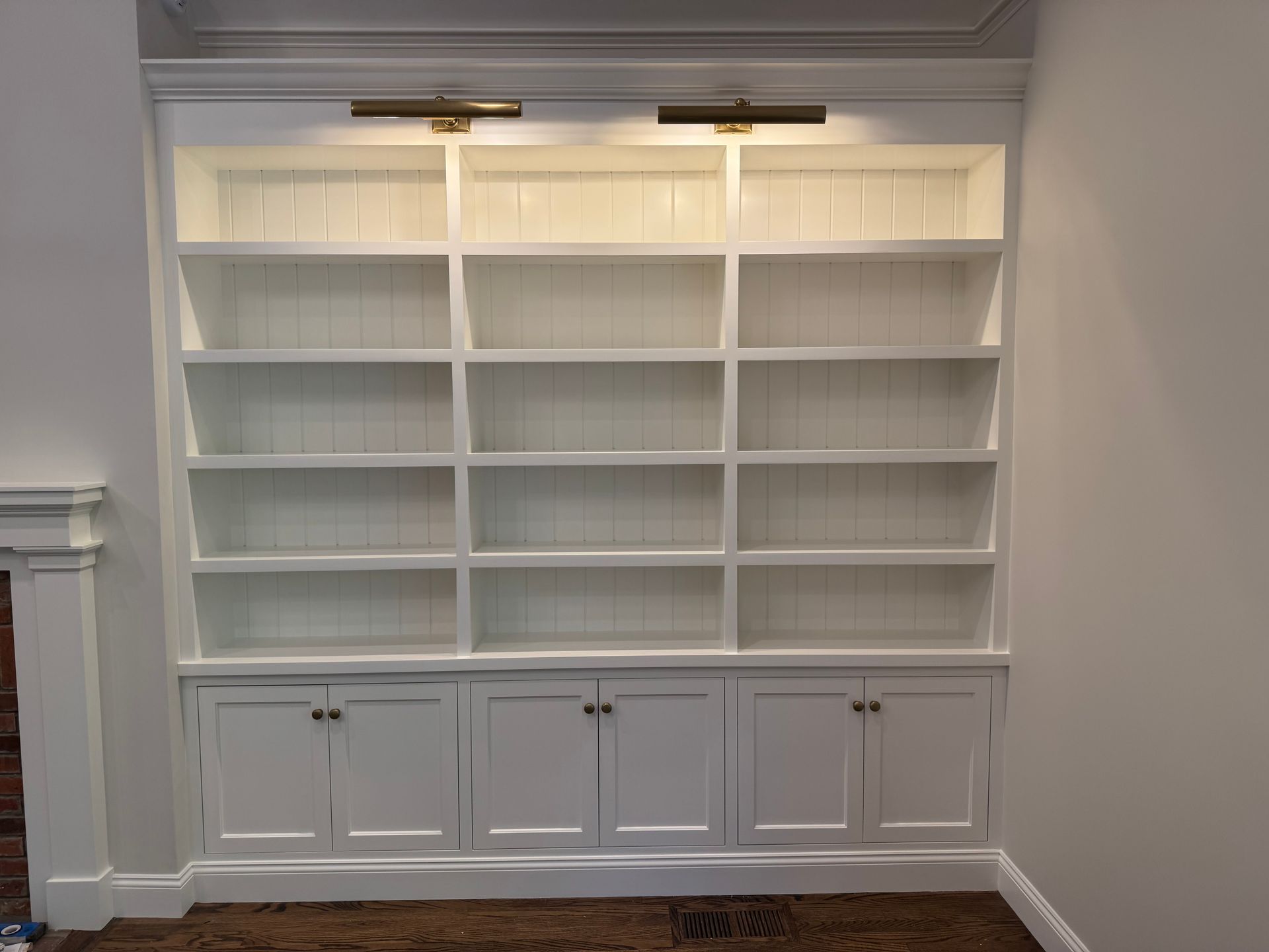 White built-in bookshelf with cabinet doors and two overhead lights.