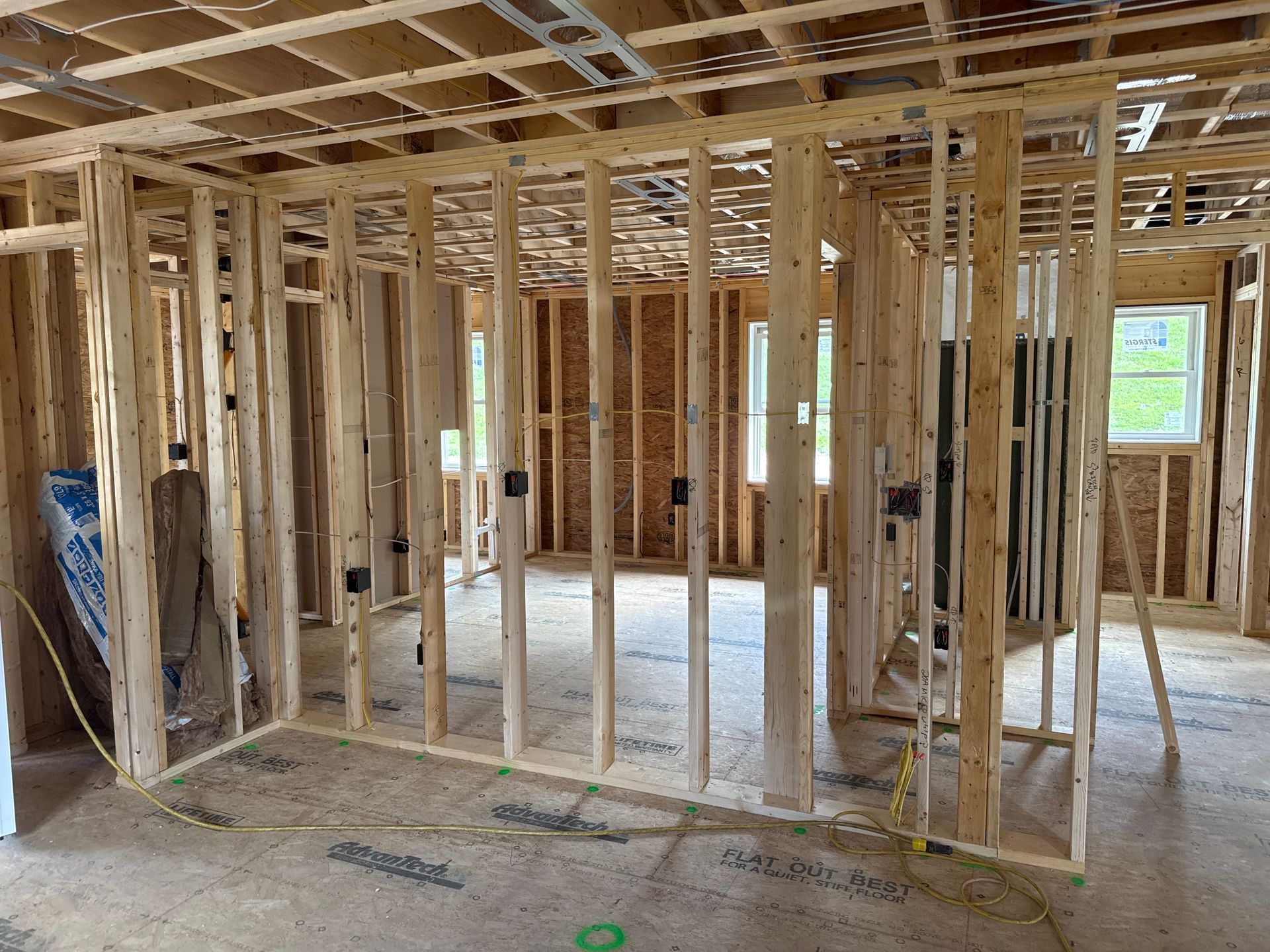 Interior wooden framing of a building under construction, showing walls, ceiling supports, and electrical boxes.
