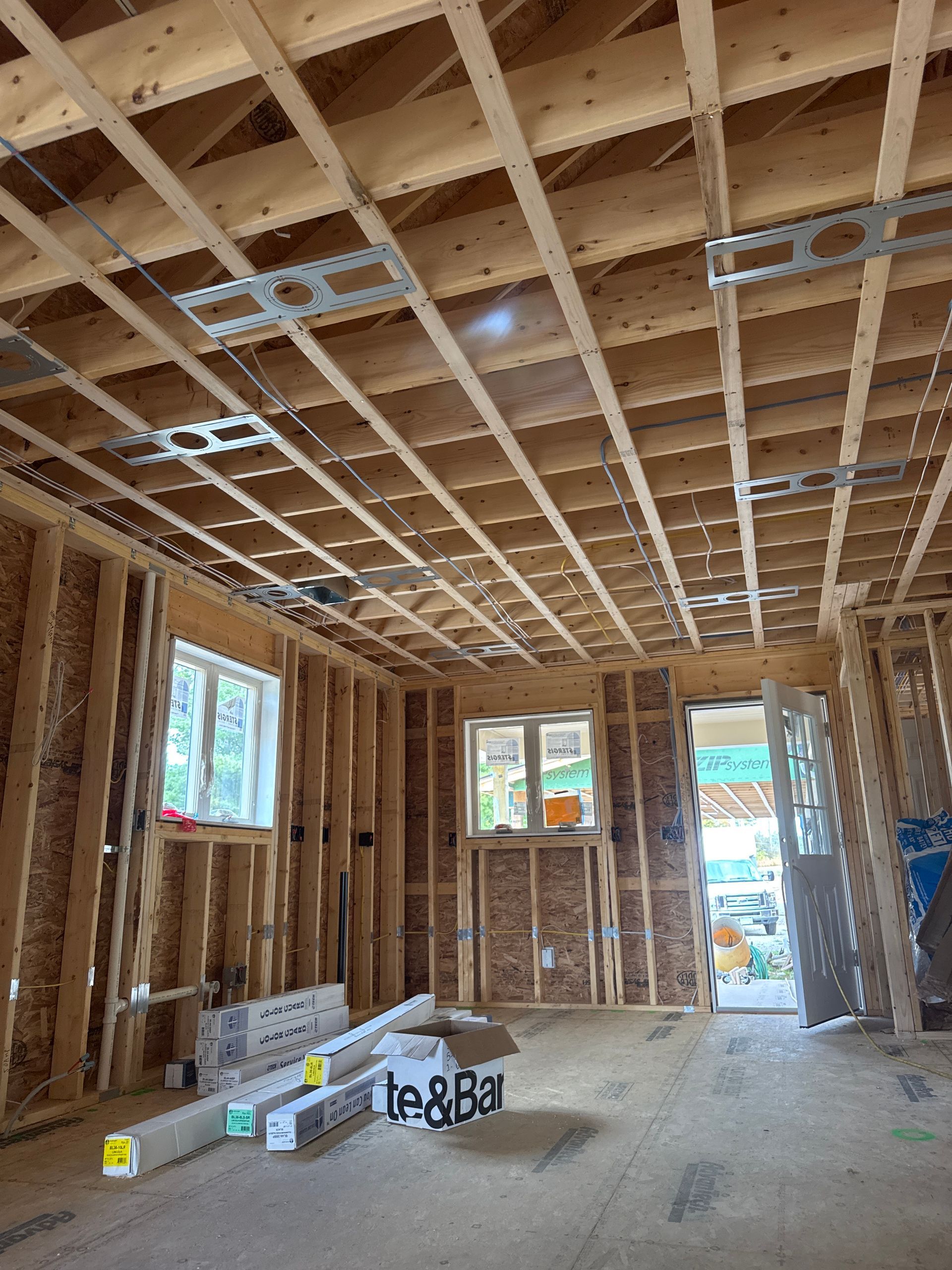 Interior of a wood-framed building under construction, showing ceiling and wall studs, and windows.