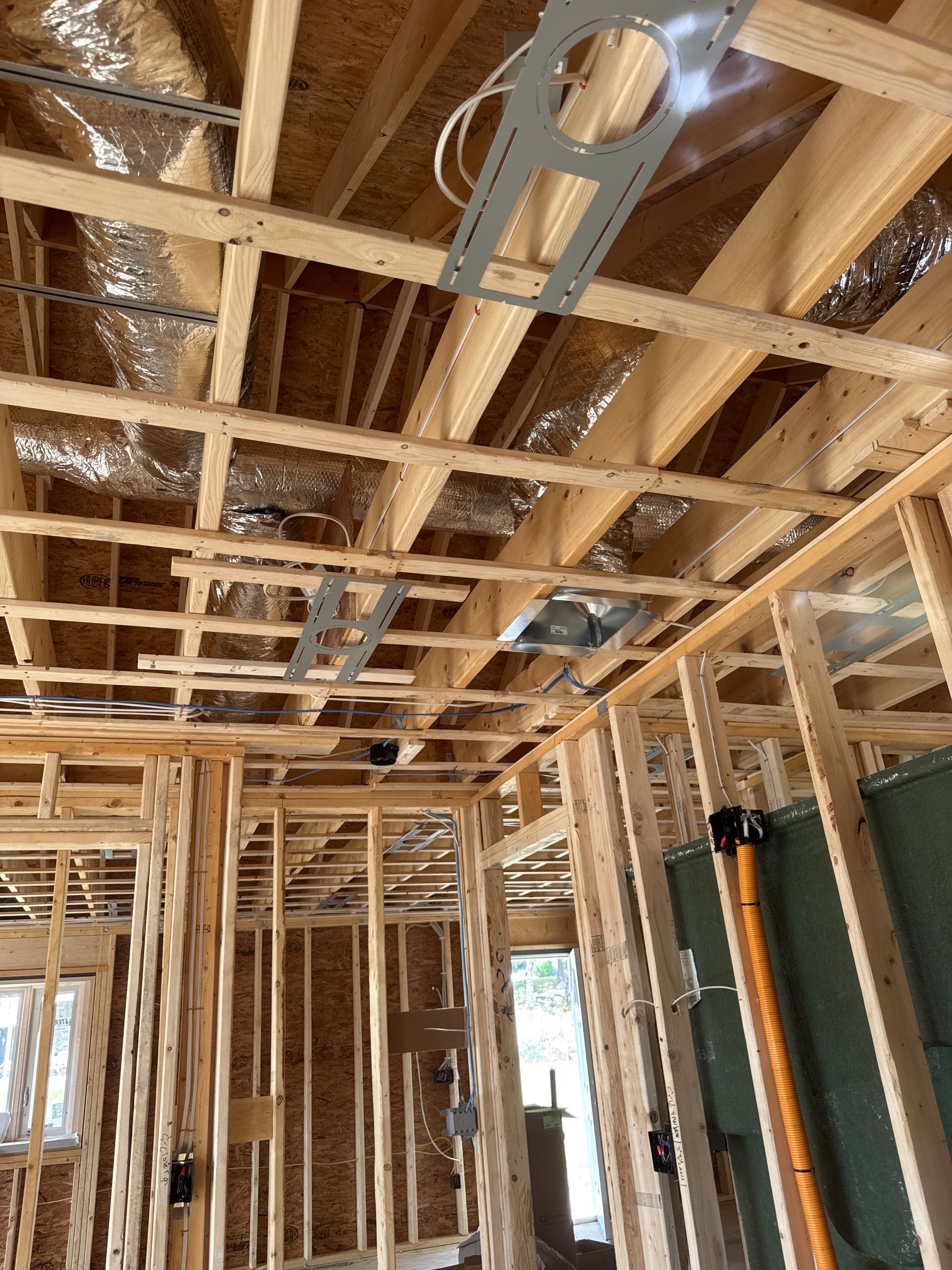Interior view of a building under construction, showing wooden framing, ductwork, and electrical wiring in the ceiling.