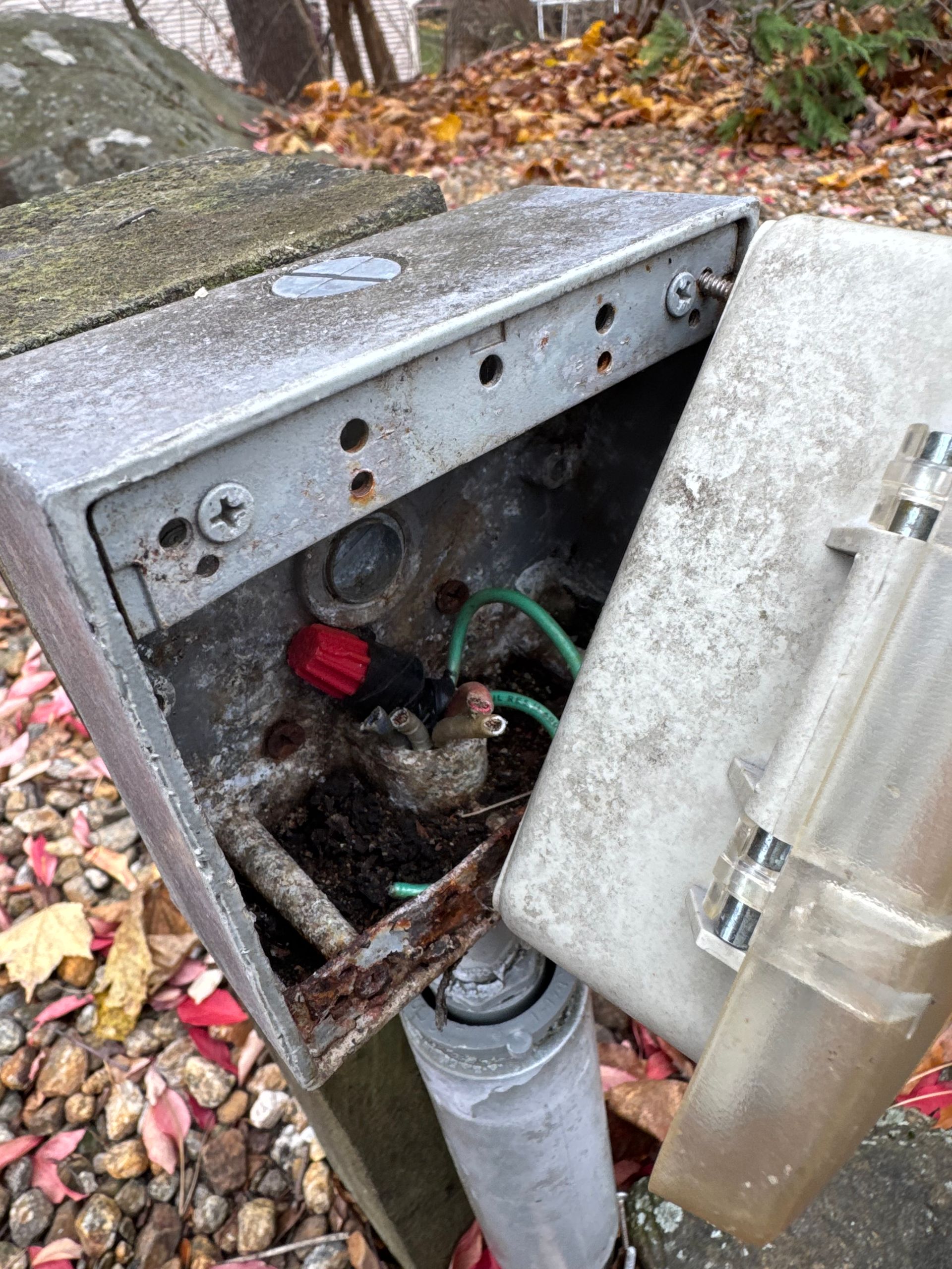 Open metal electrical box on a pole, showing wiring and rust, with the cover ajar.