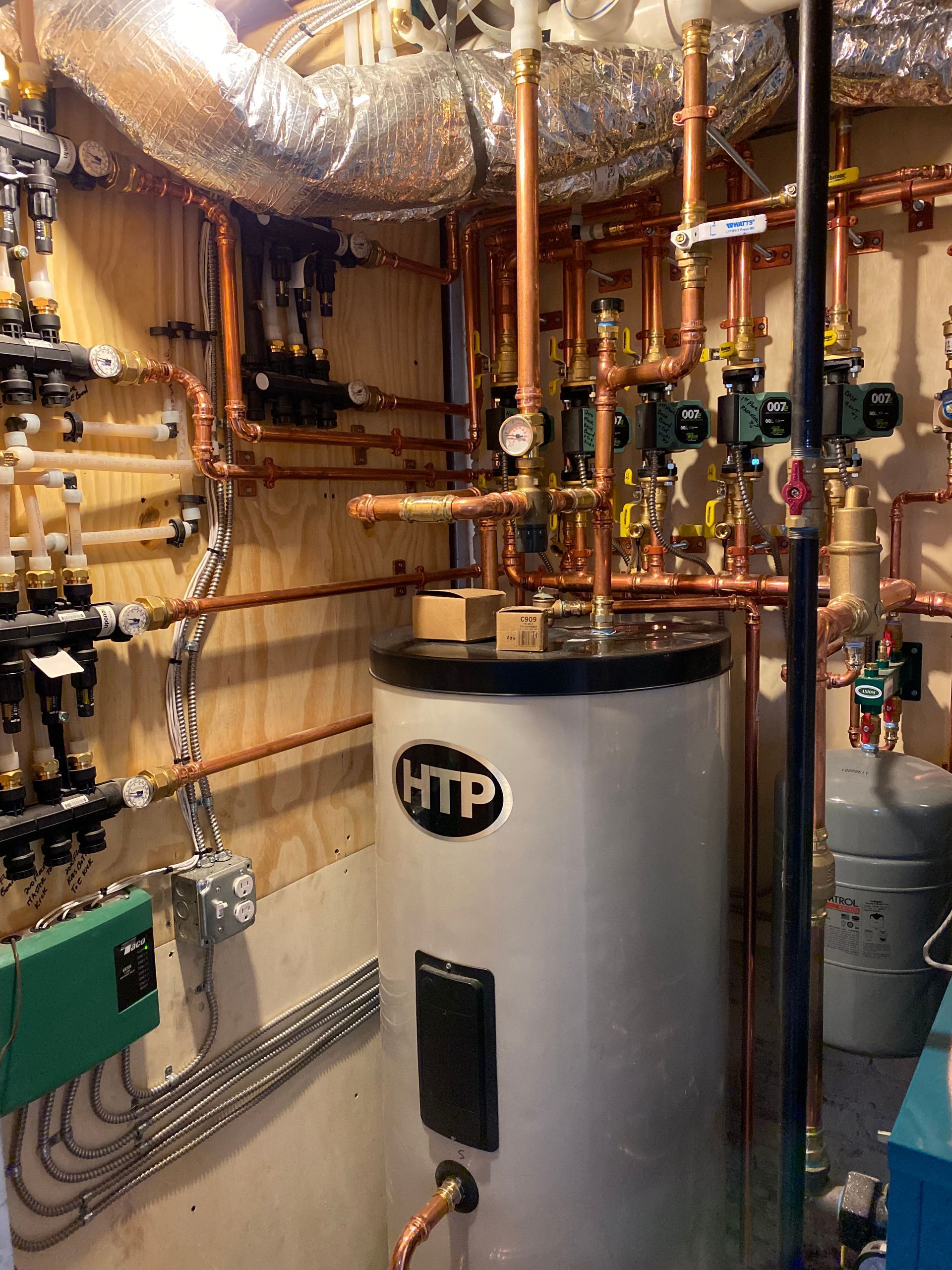 Copper pipes and valves surrounding a white HTP water heater in a utility room.