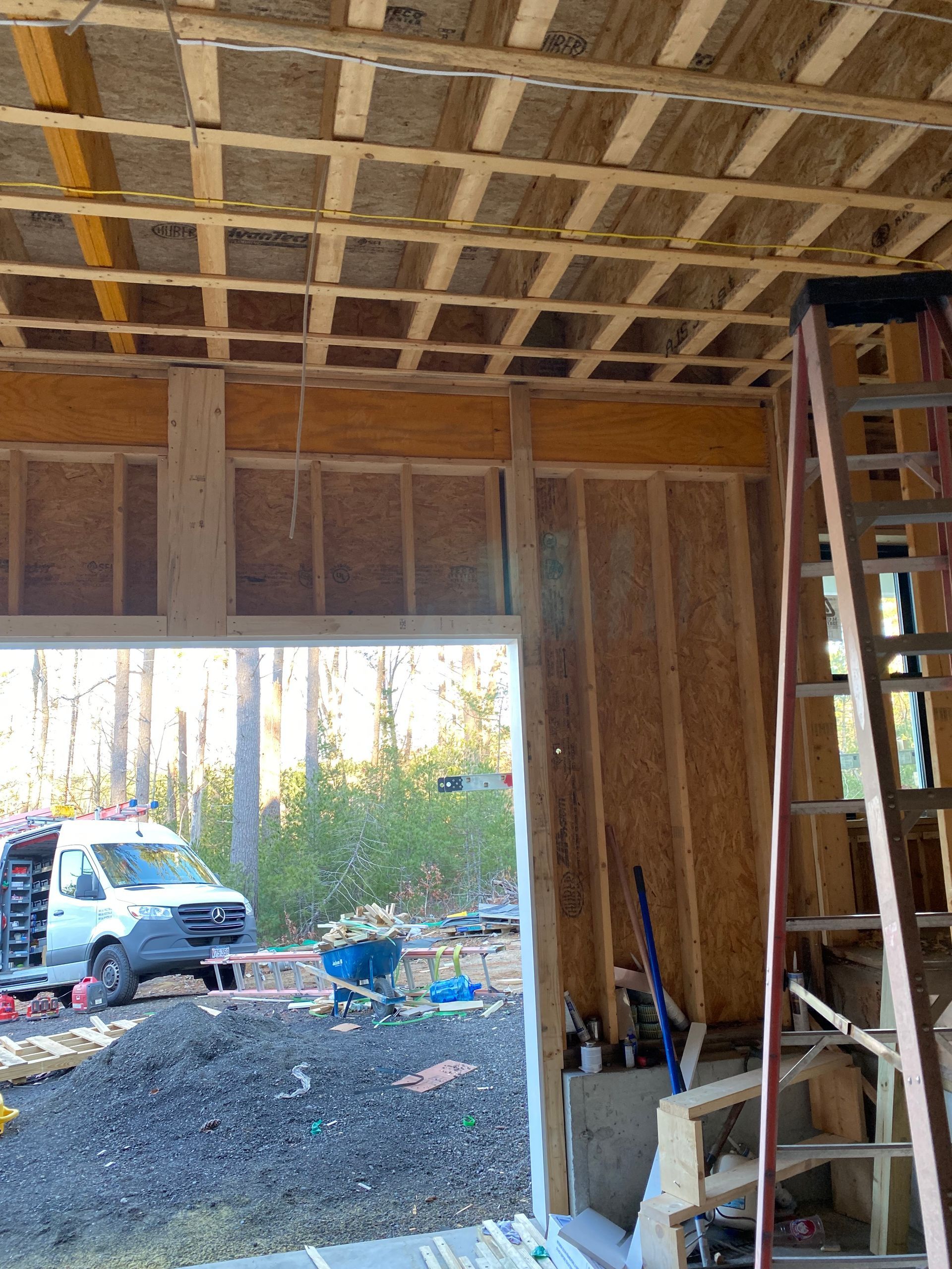 Construction site: wooden frame with open doorway, ladder, ceiling framing, and a white truck.