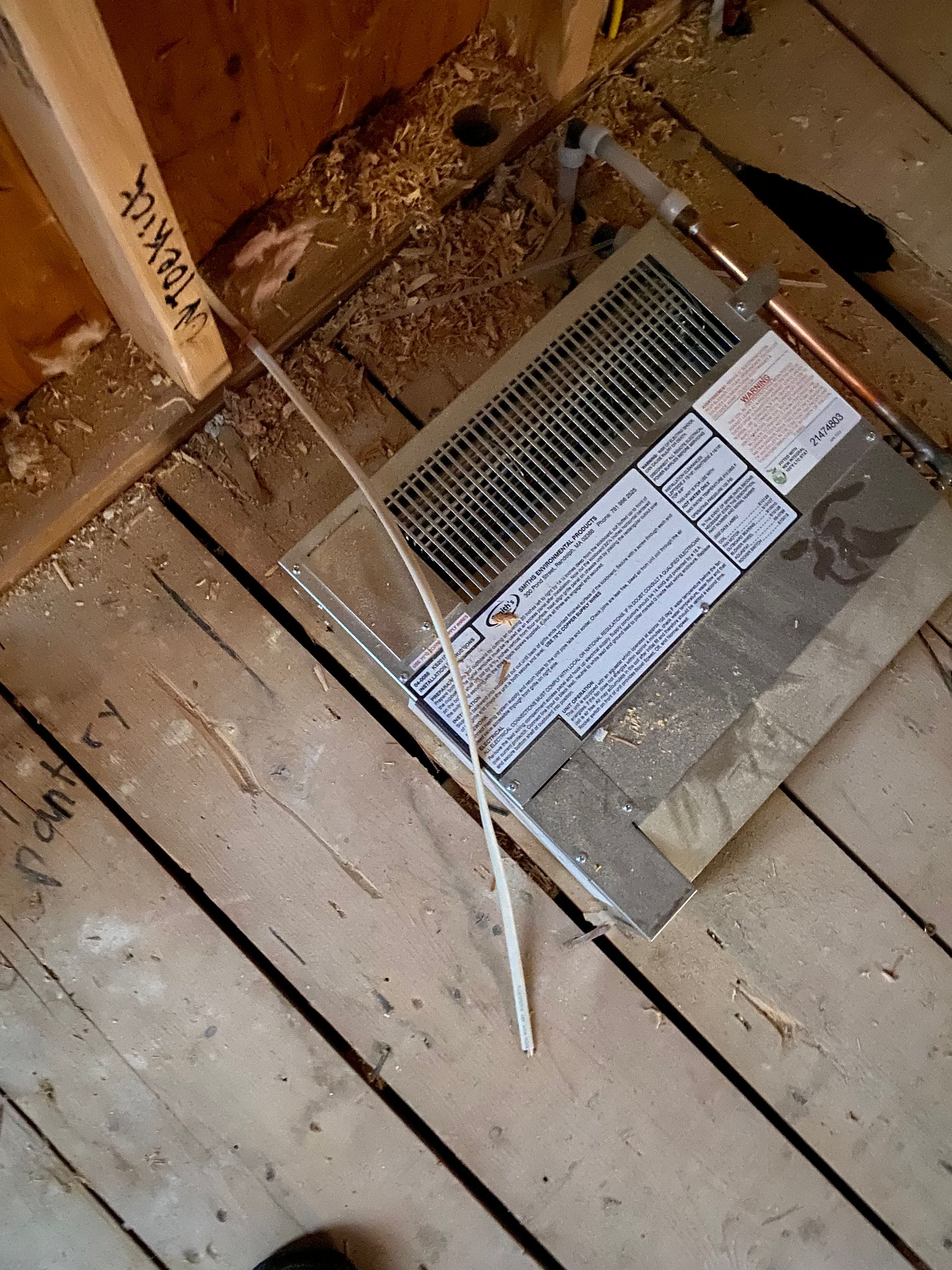 HVAC vent cover on wooden floor in construction setting. A thin, white pipe is lying across.