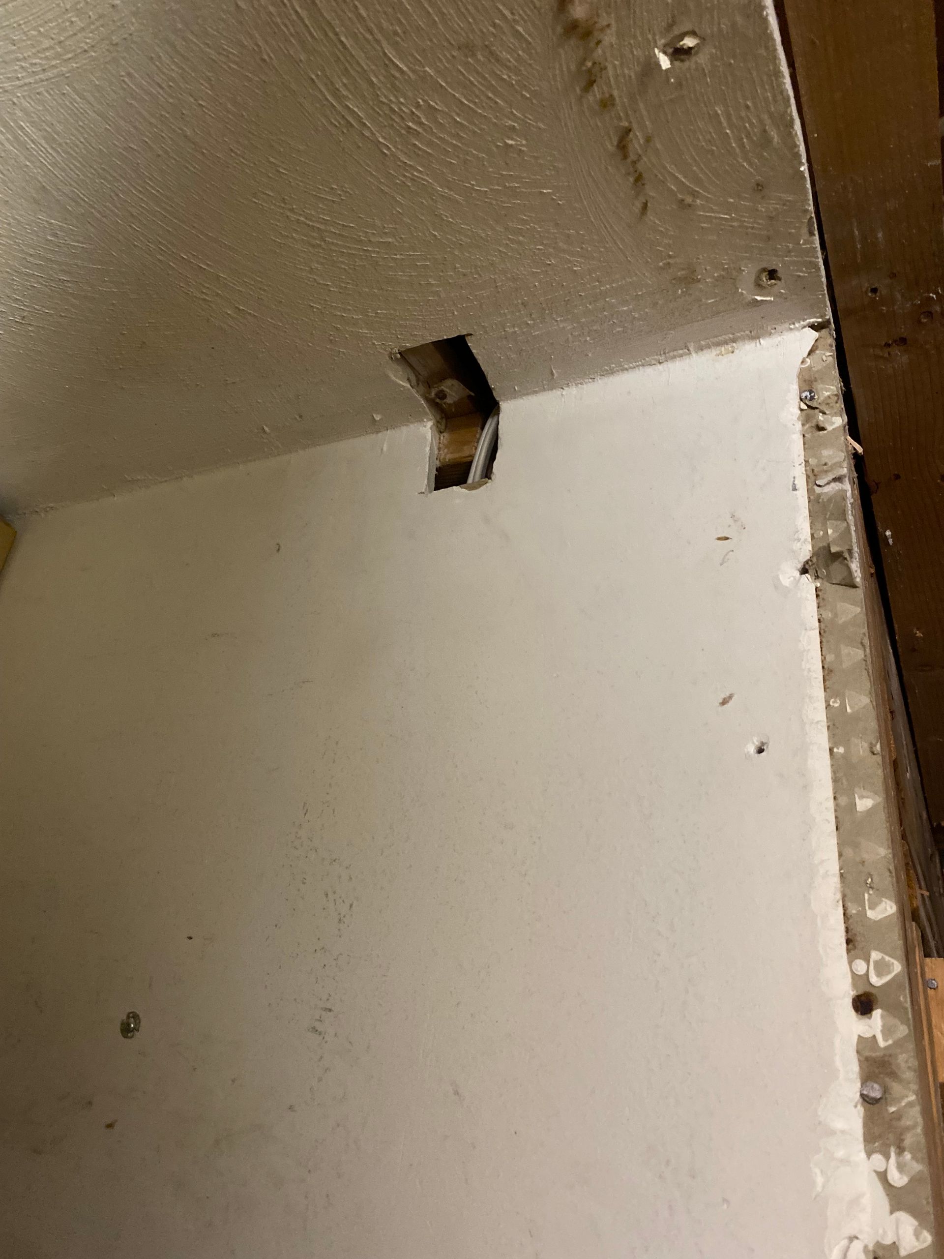 White wall with a rectangular hole near the ceiling; a metal bracket is visible in the hole.