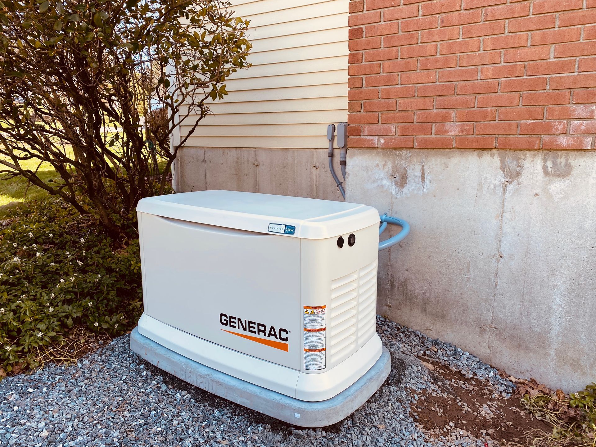A Generac home generator next to a beige-sided house and red brick wall.