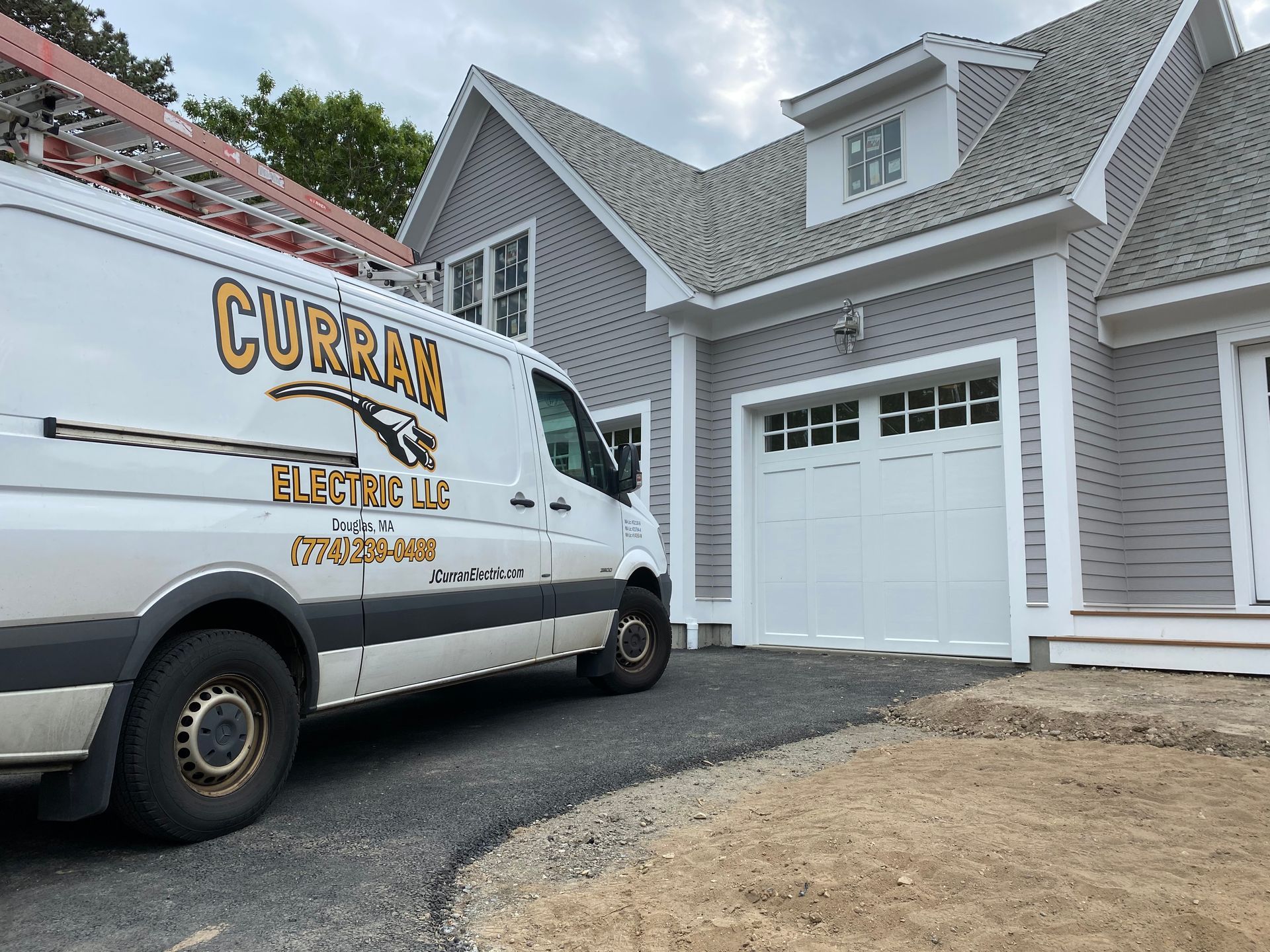White Curran Electric van parked on driveway in front of a gray house with a white garage door.