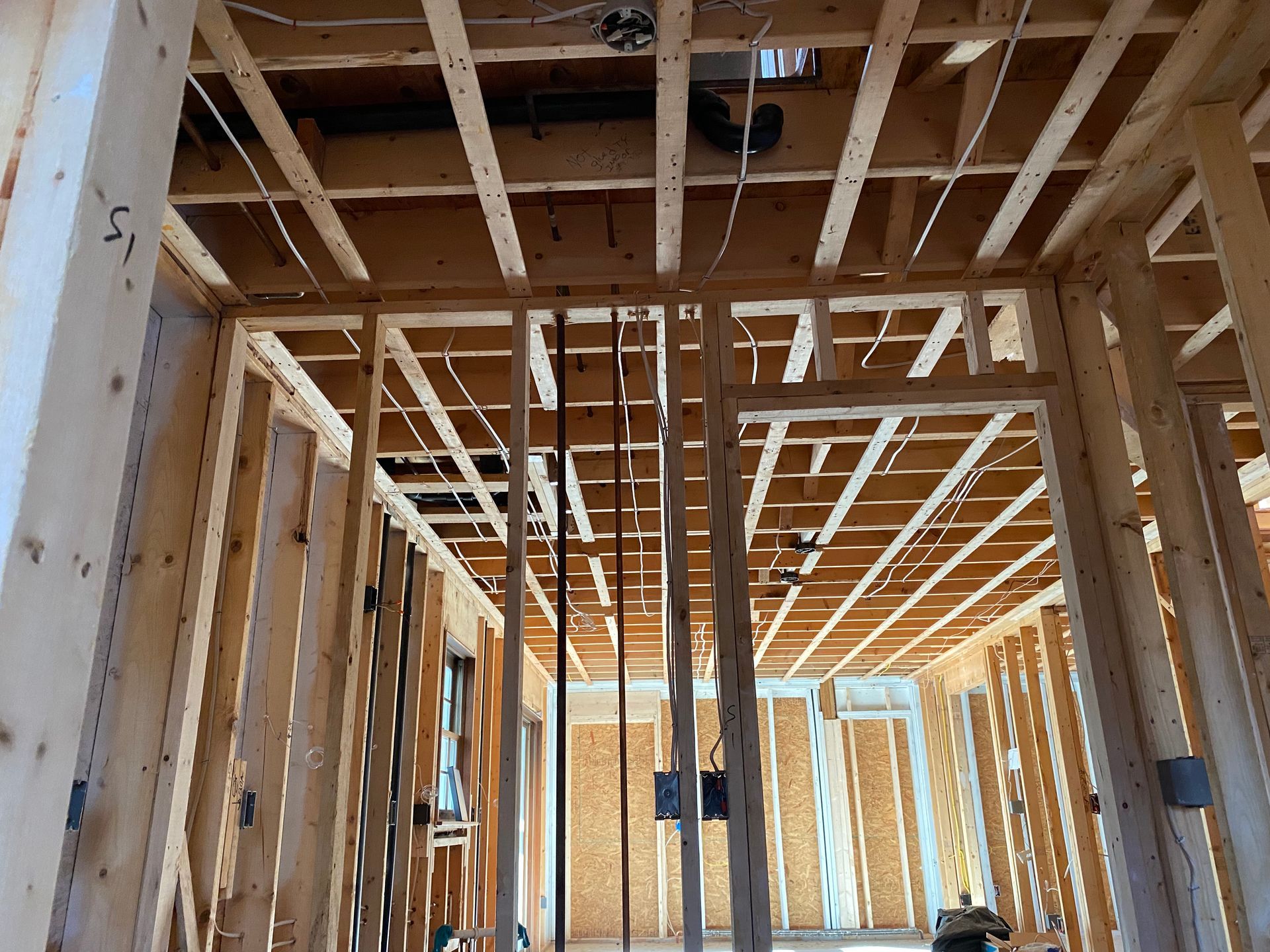 Interior view of a building under construction, showing wooden framing for walls and ceiling; electrical wiring visible.