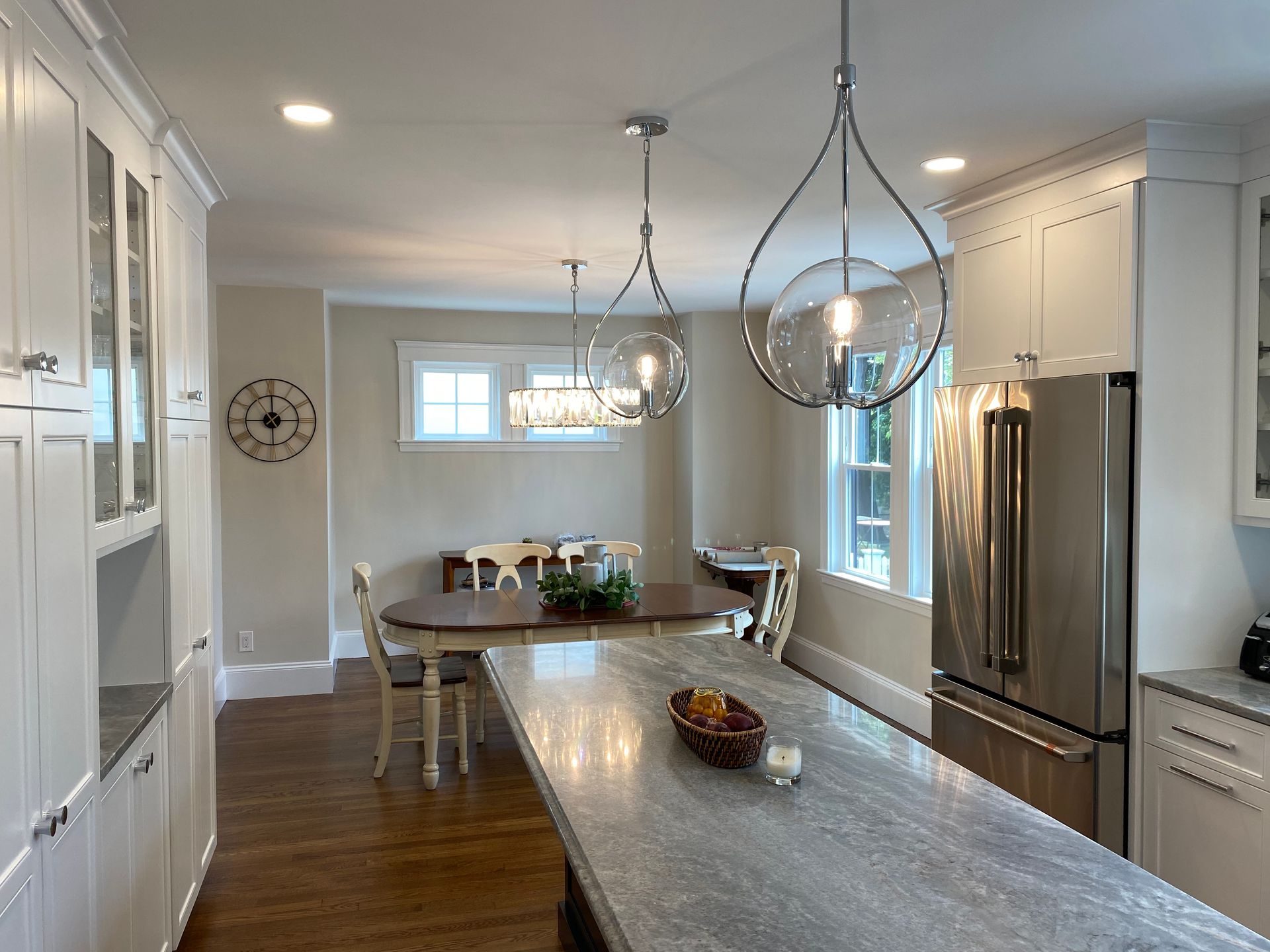 Kitchen with white cabinets, island with gray countertop, dining table, and stainless steel refrigerator.
