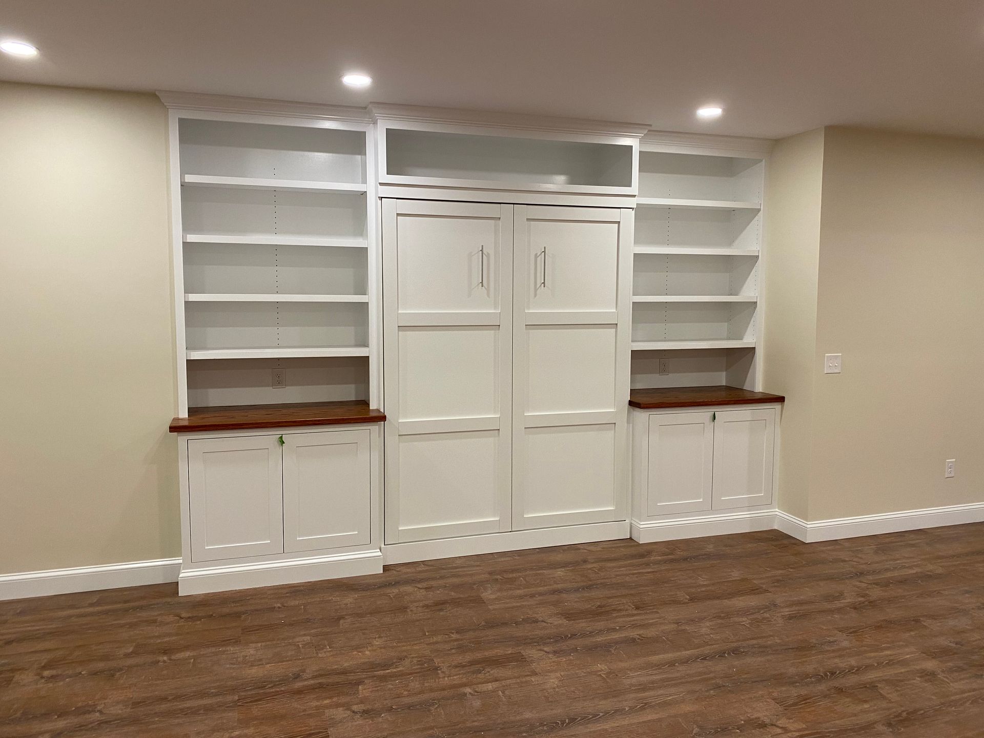 Built-in white cabinets with bookshelves flanking a center unit; brown carpet, beige walls.