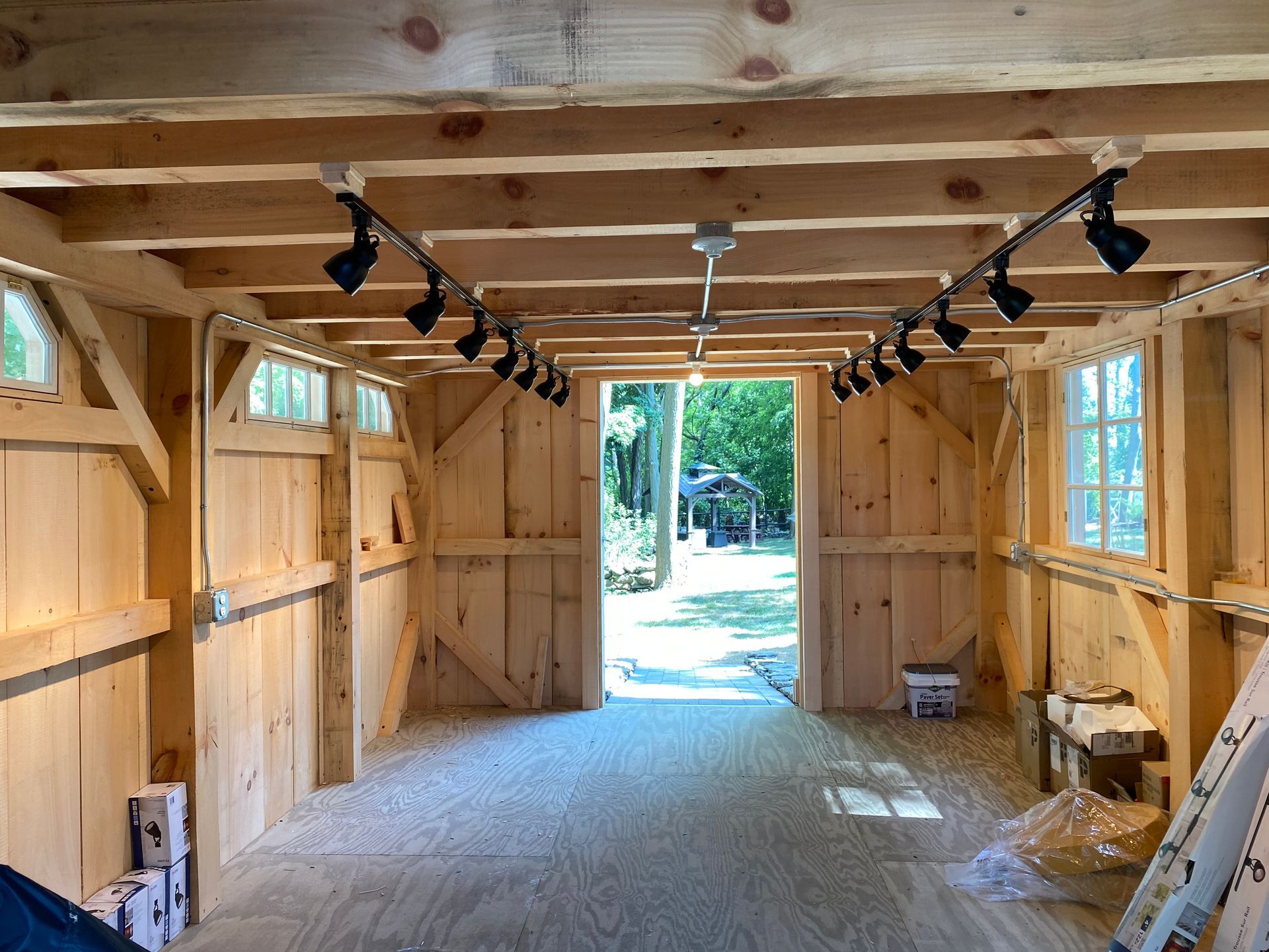 Interior of a wooden building with open doors, track lighting, and small windows. Natural light and wood tones.
