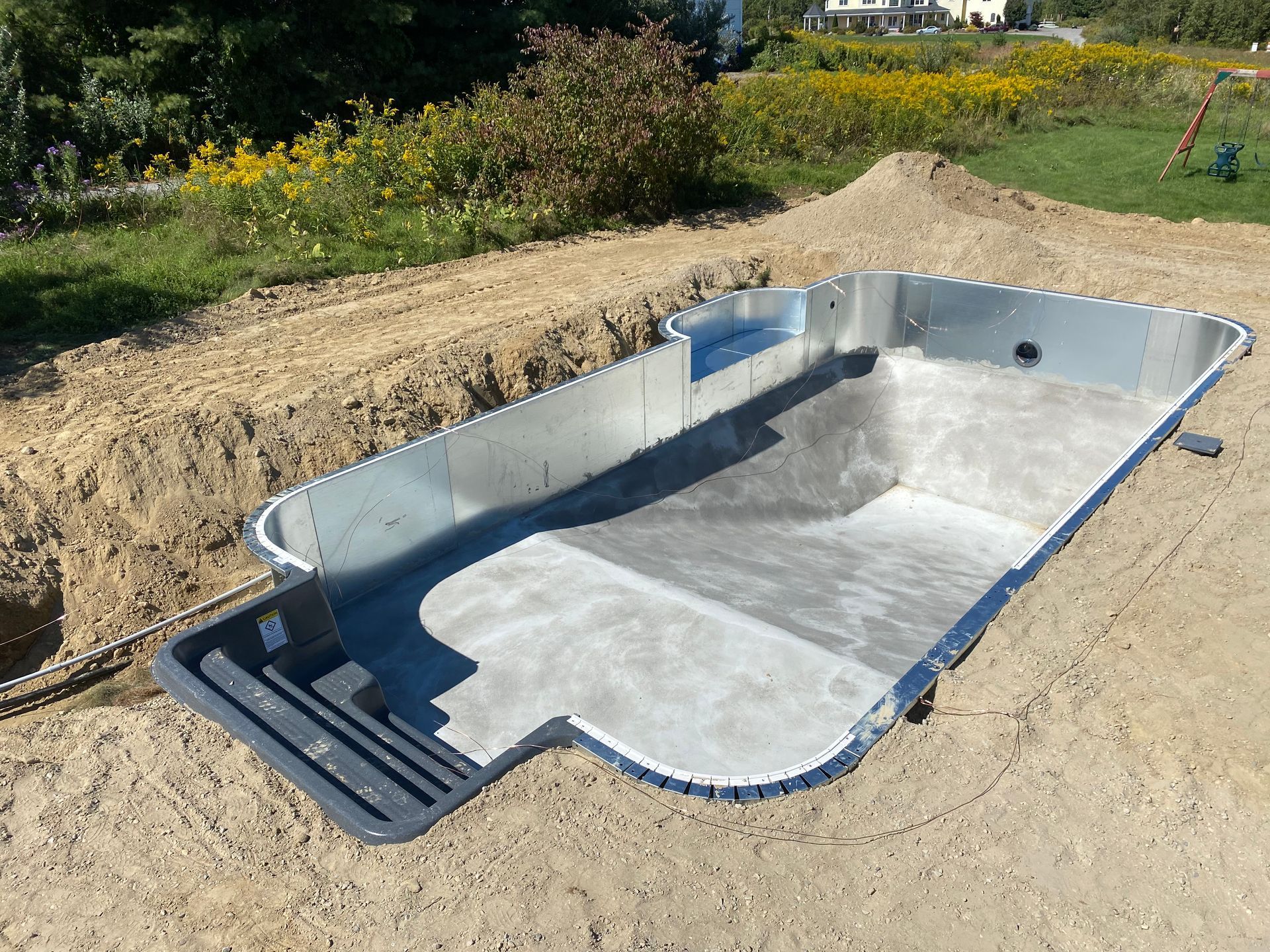 Concrete swimming pool shell in a dirt excavation, waiting for construction.