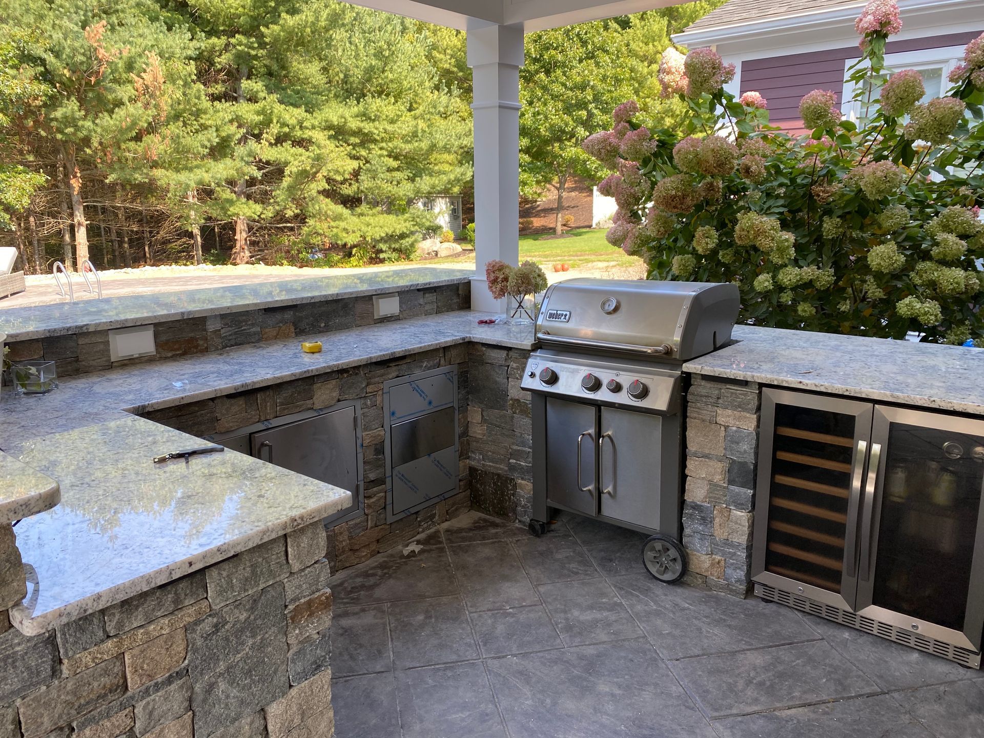 Outdoor kitchen with granite countertops, stainless steel grill, and stone facade.