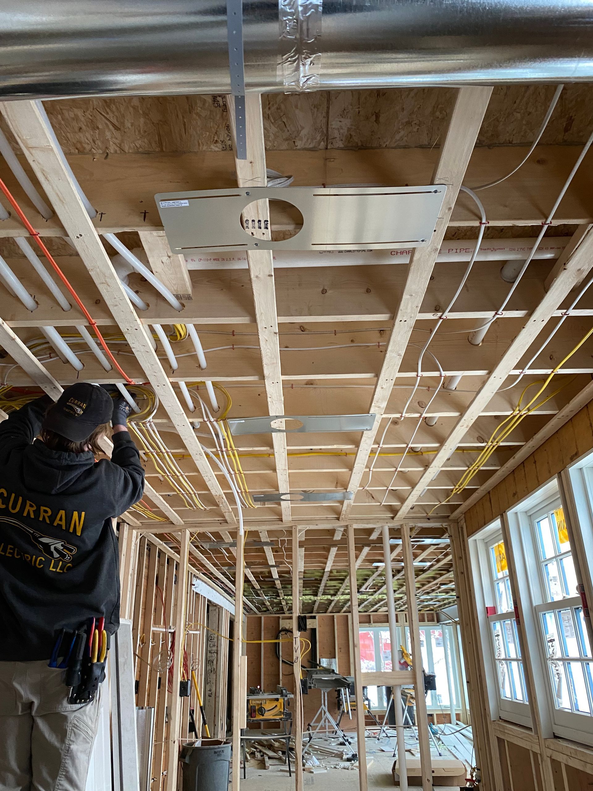 Construction worker installs electrical wiring in a room with exposed framing and ductwork.