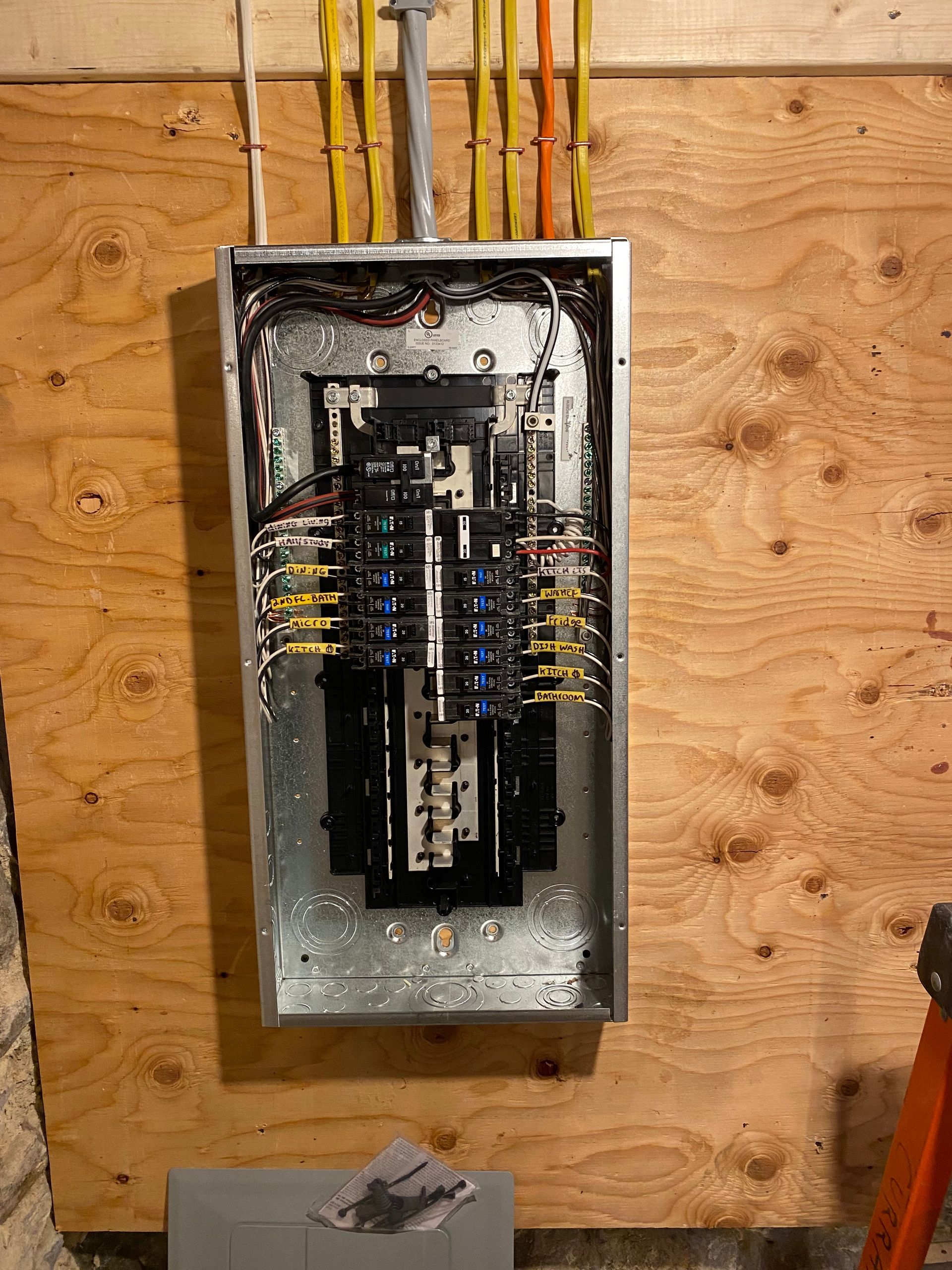 Electrical panel installed on a plywood wall, wires entering from above, interior exposed.