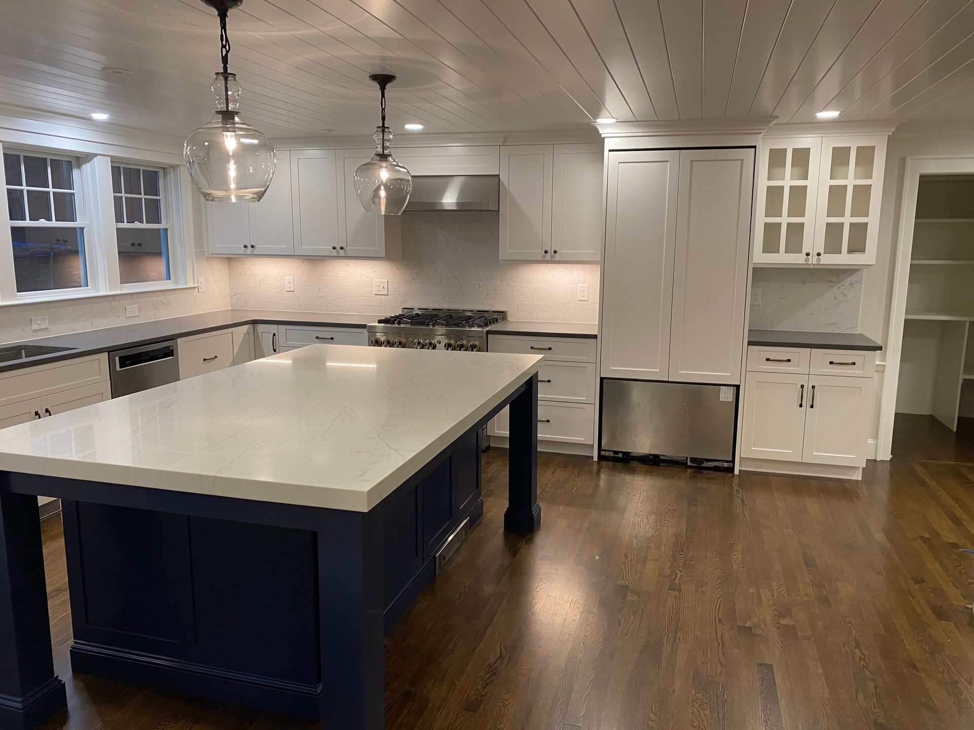 Modern kitchen with white cabinets, dark blue island, stainless steel appliances, and dark wood floors.
