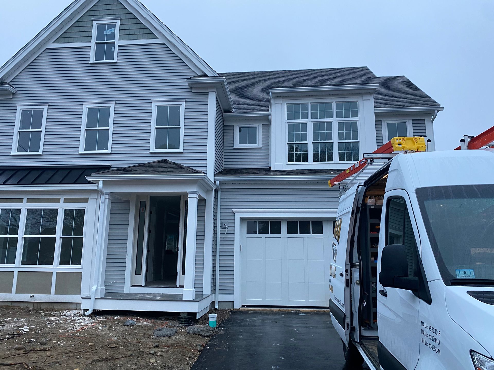 Two-story gray house with white trim and a white garage door. A work van is parked in front.