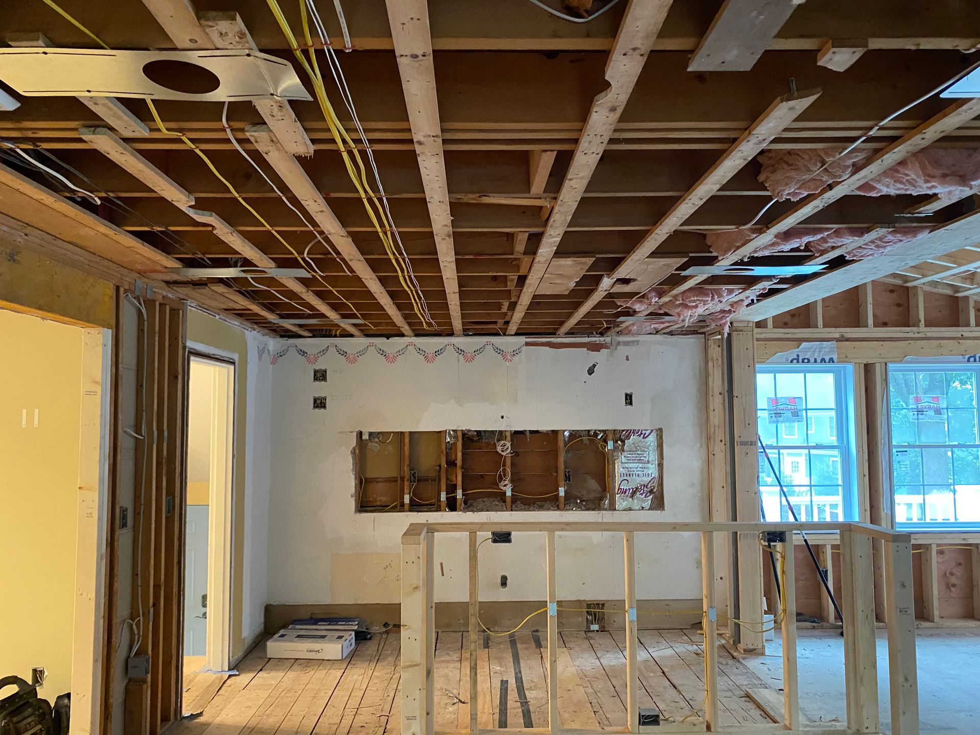 Interior view of a room under construction with exposed ceiling beams, wiring, and framing.