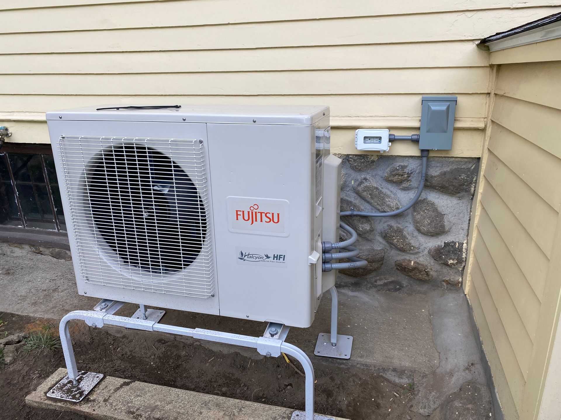 Fujitsu heat pump unit mounted on a concrete slab next to a building wall.